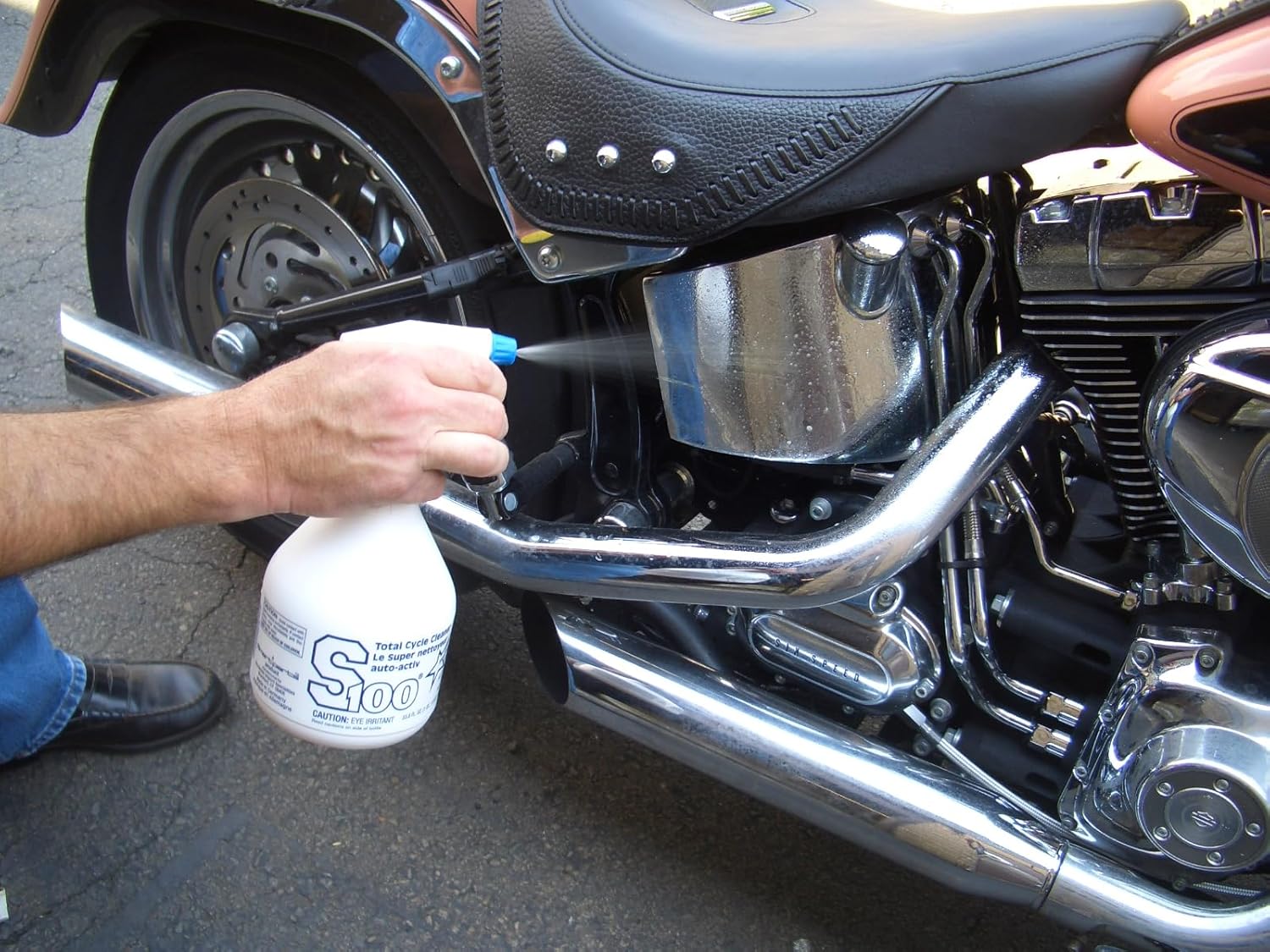 Hand spraying S100 cleaner onto a motorcycle engine
