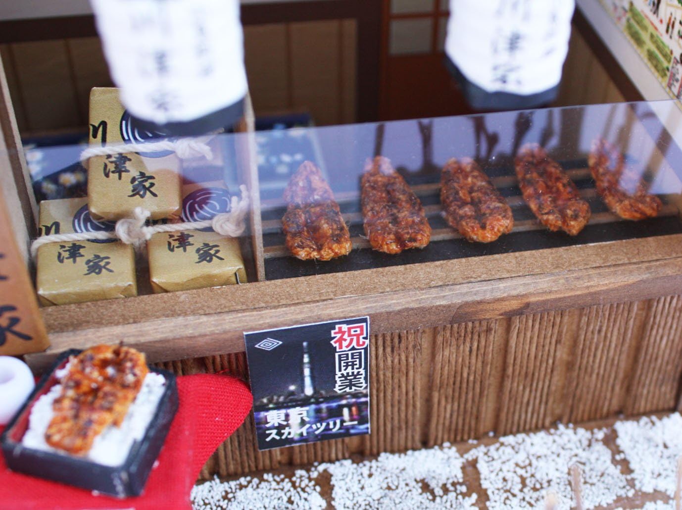 Close-up view of the miniature eel dishes and packaging inside the Shibamata Eel Shop dollhouse kit.