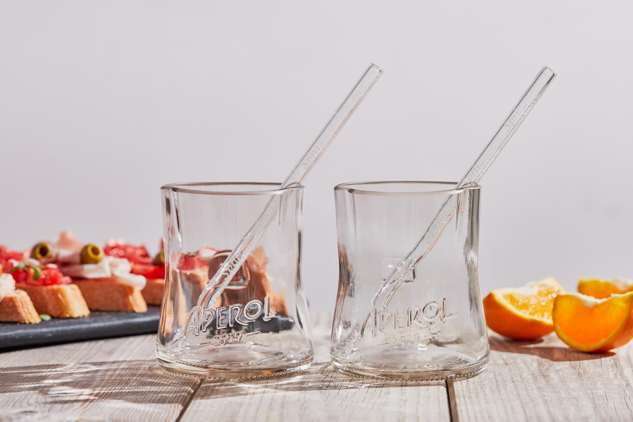 Aperol Spritz Set aus recycelten Flaschen: zwei Glaser mit kunstvoll geformten Randern und zwei Glasstronhhalme