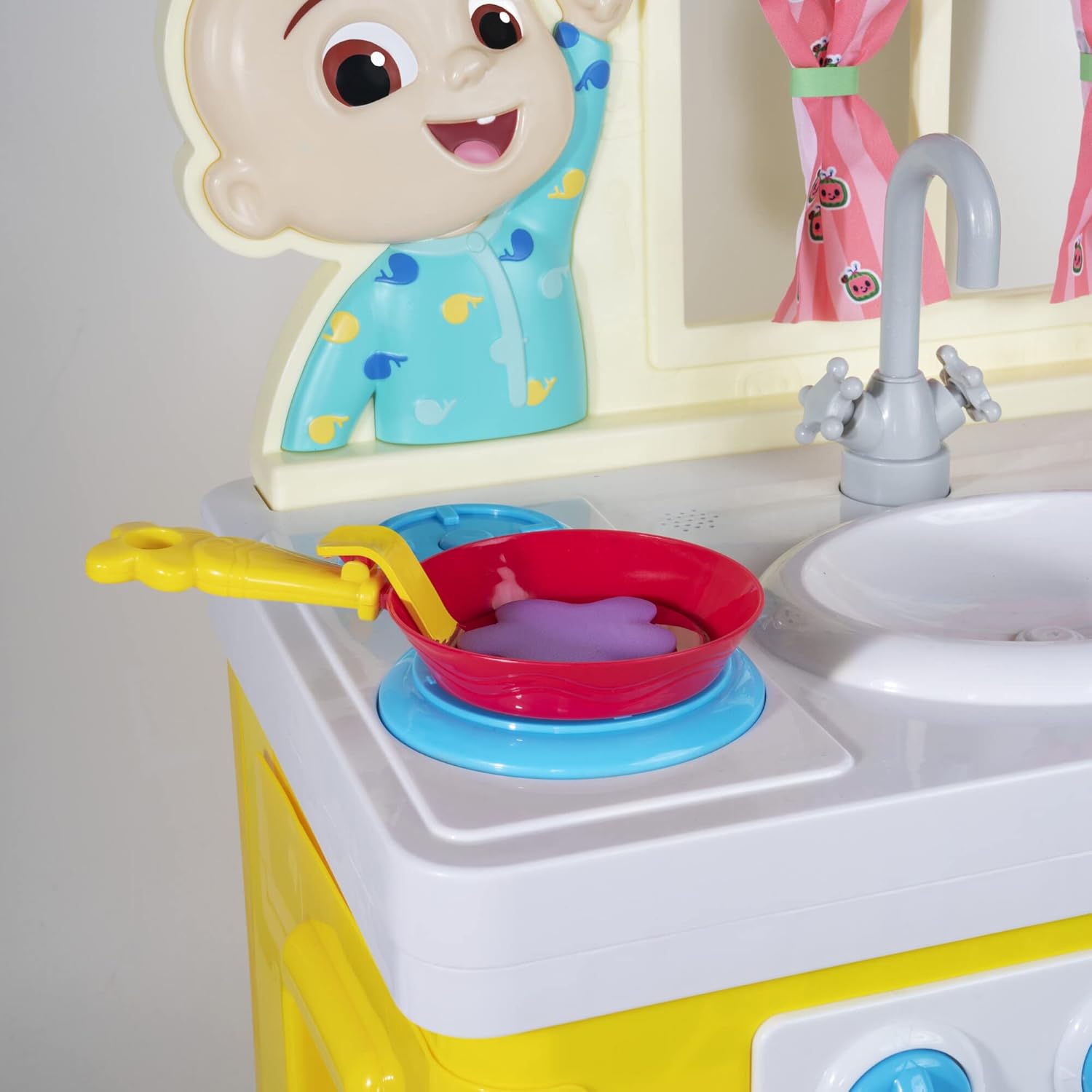 Close-up of the CoComelon kitchen stove with a red frying pan on a blue burner, showing the interactive knobs.