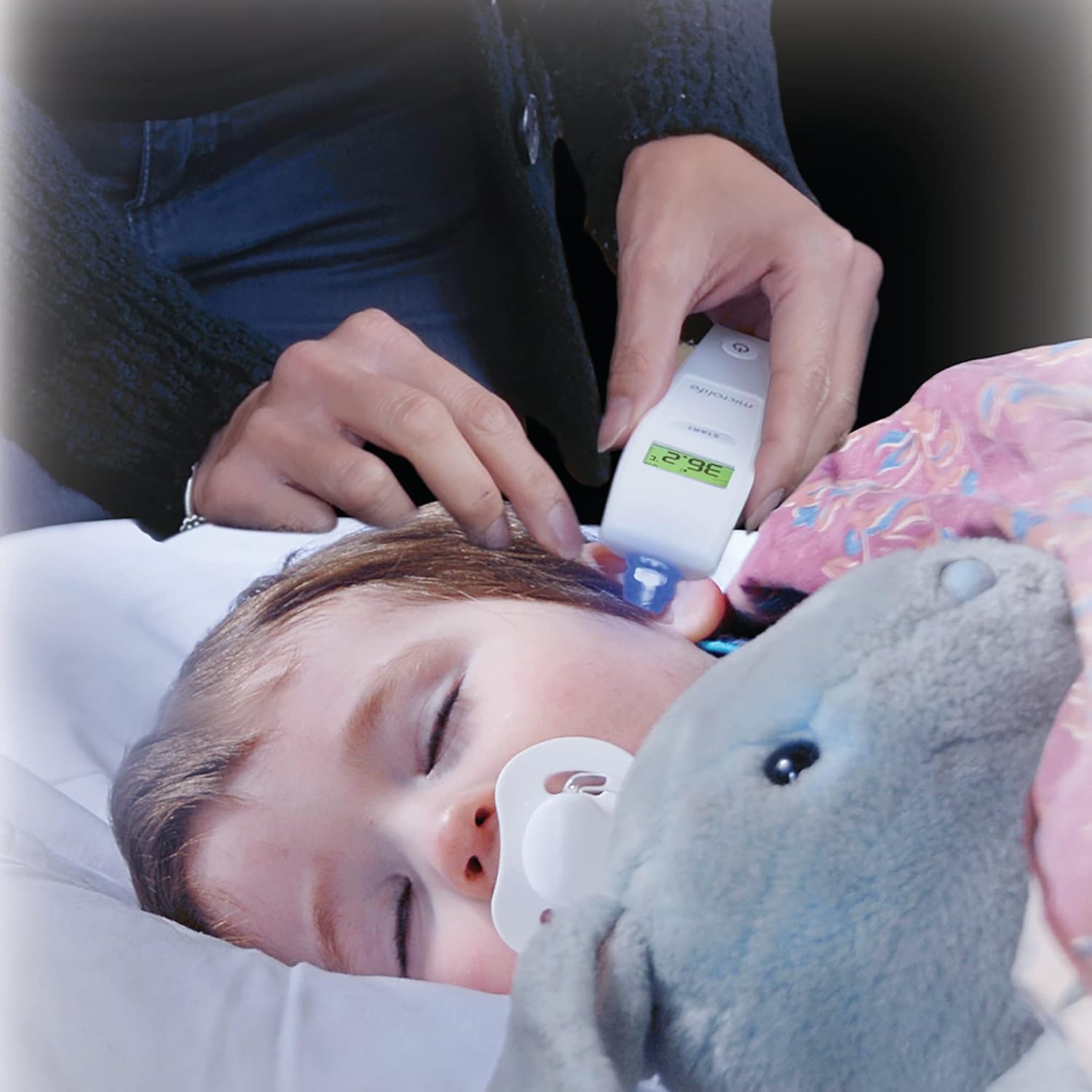 Person taking temperature of a sleeping child with ear thermometer