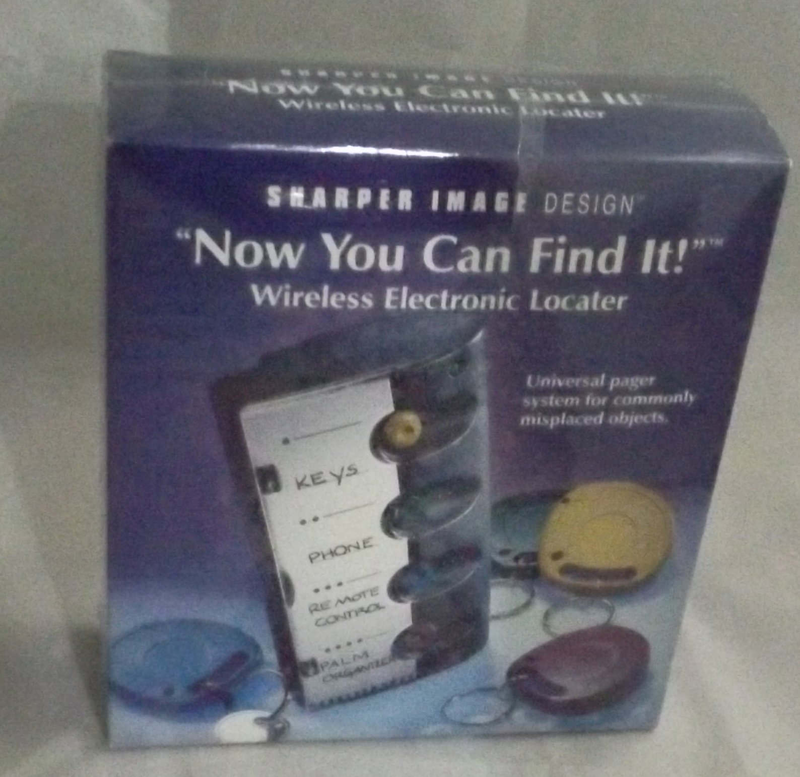 Sharper Image Wireless RF Electronic Locator packaging showing the base unit and a blue receiver disc with a key.