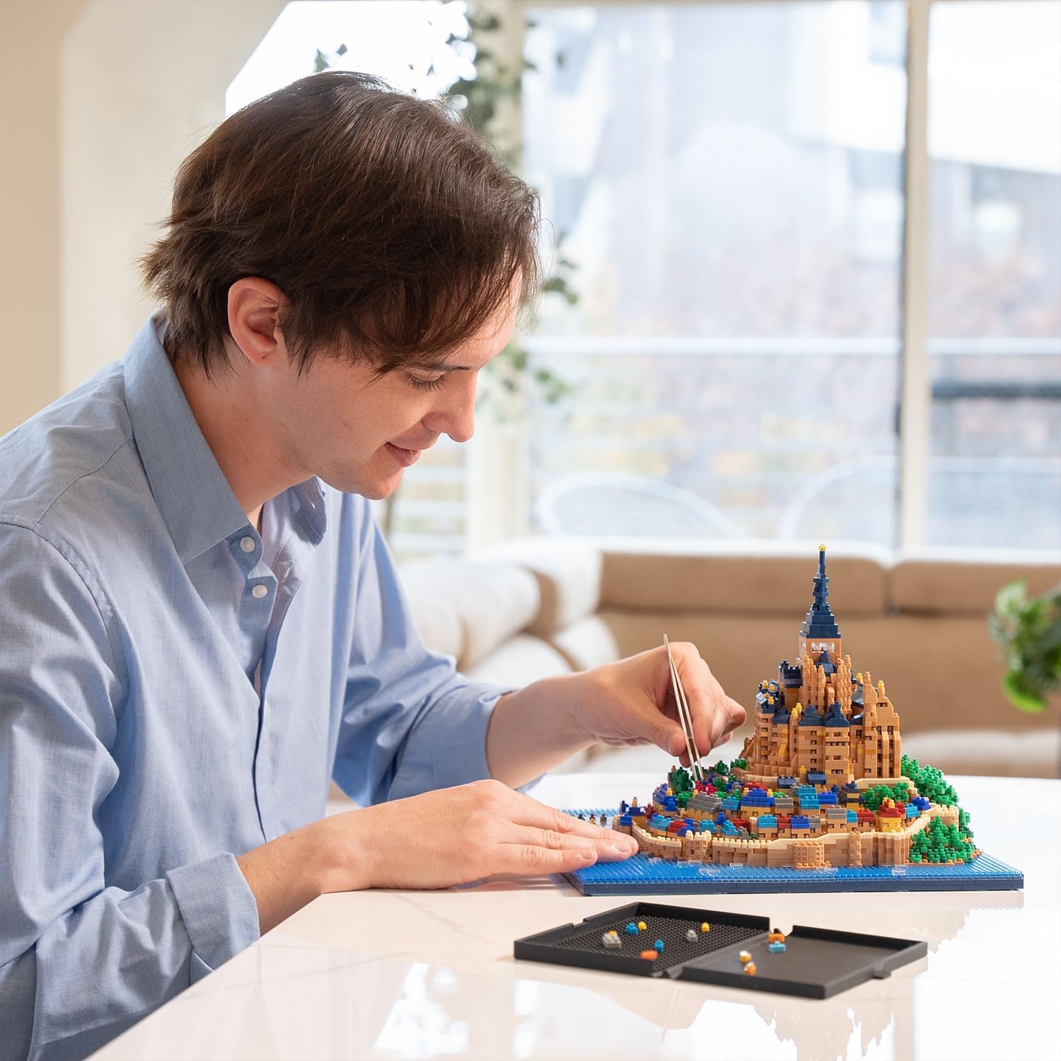 A person carefully assembling the nanoblock Mont Saint-Michel model using small tools.