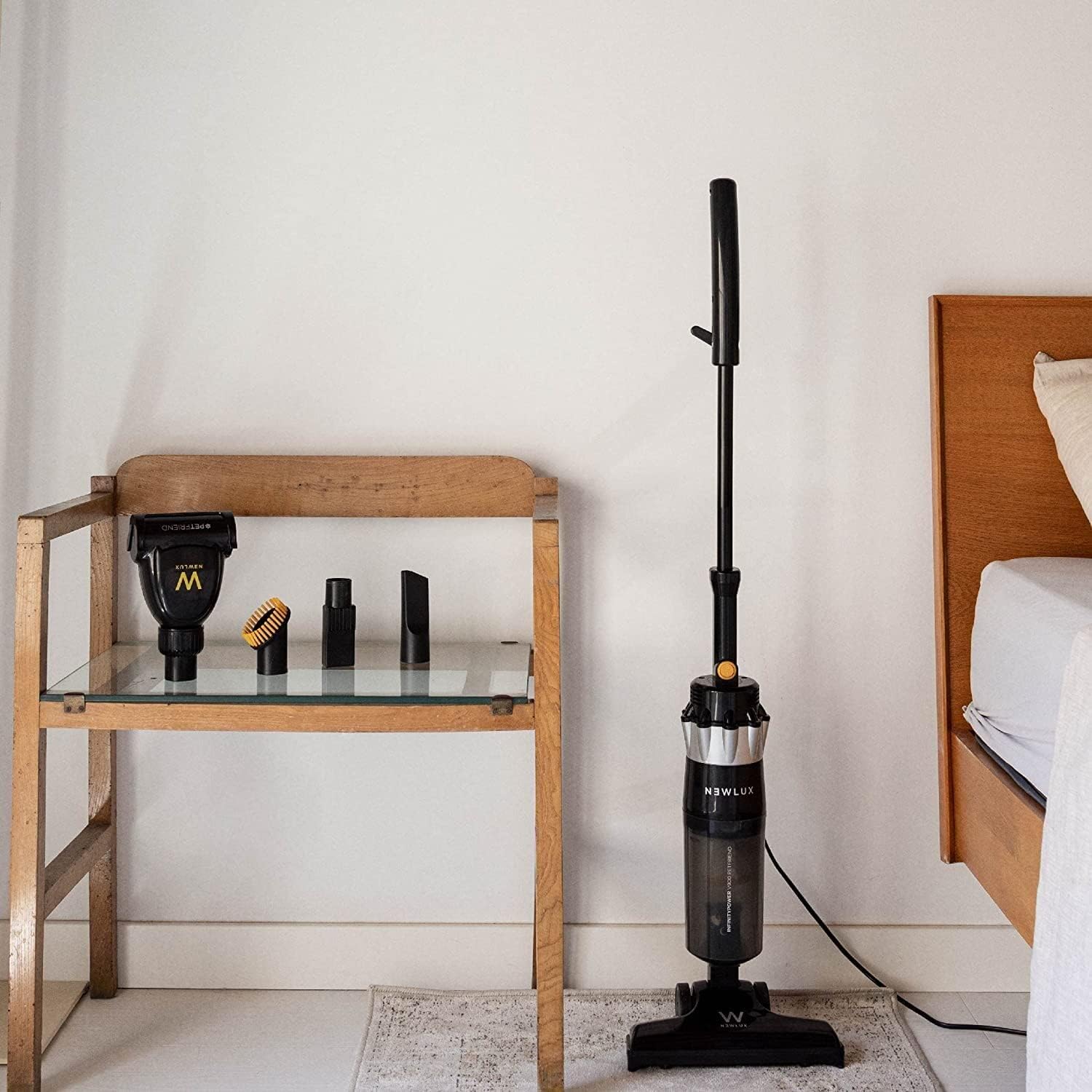 NEWLUX V900 vacuum cleaner in its upright stick configuration, standing next to a wooden table with accessories.