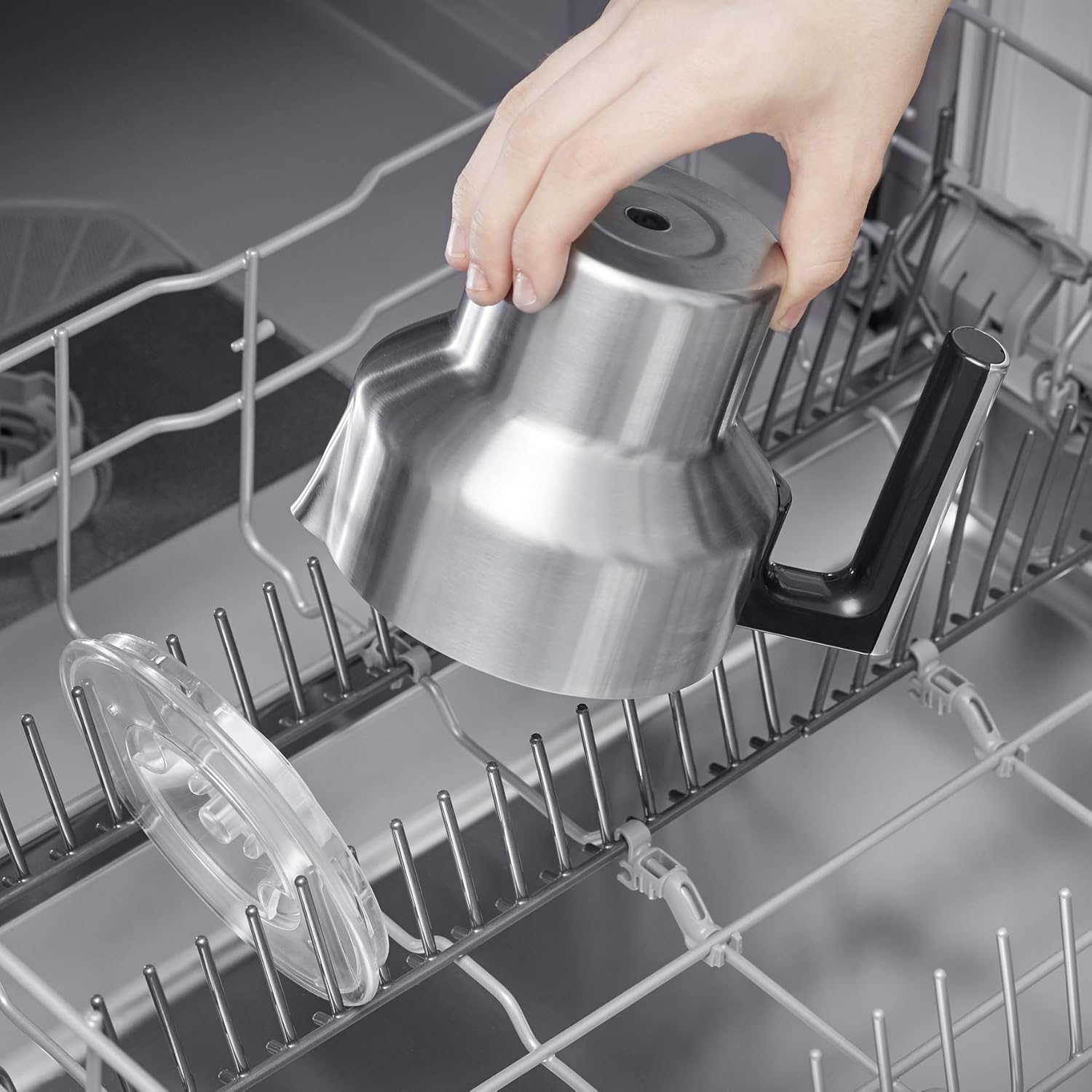 Stainless steel milk frother jug and lid being placed in a dishwasher