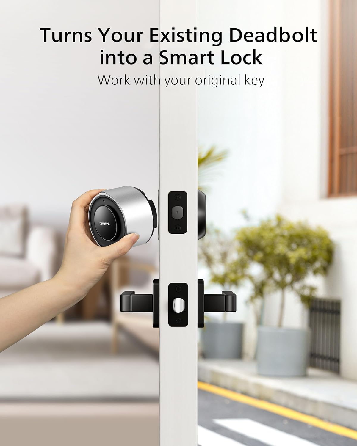 Hand holding the Philips Smart Lock next to an existing deadbolt on a door, illustrating the retrofit process.