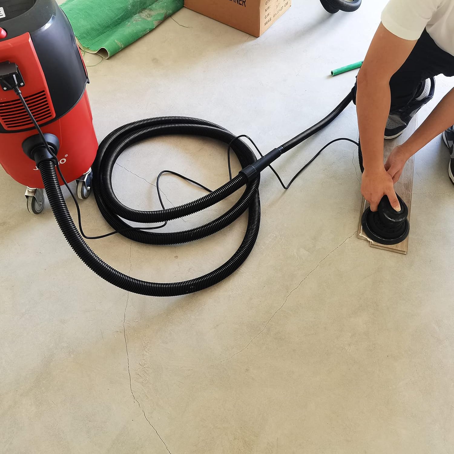 A person connecting the black corrugated hose to the inlet port of the red dust extractor