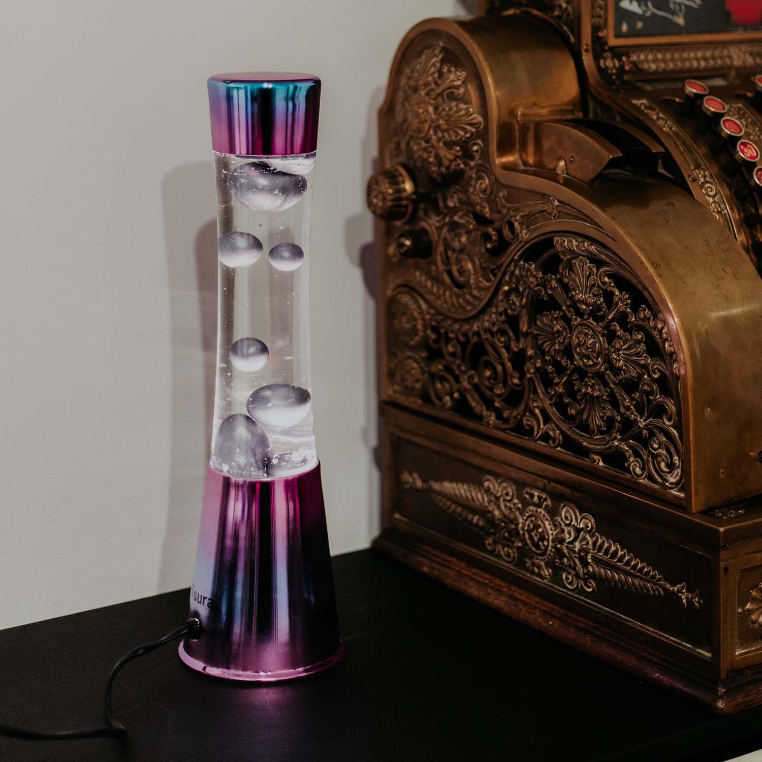Fisura - Lámpara de lava iridiscente. Base iridiscente, líquido transparente y lava morado metálico. Lámpara efecto relajante. Con bombilla de repuesto. 11 cm x 11cm x 39,5 cm.