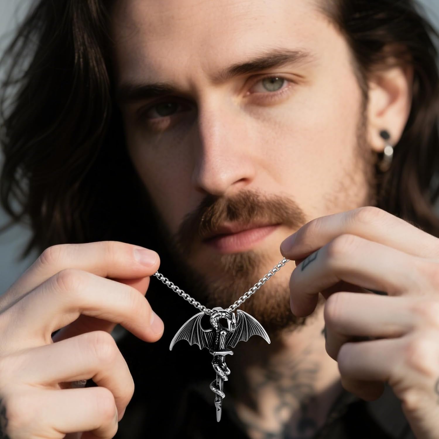 A man holding the Winged Dragon Sword necklace, demonstrating its size and how it might be worn.