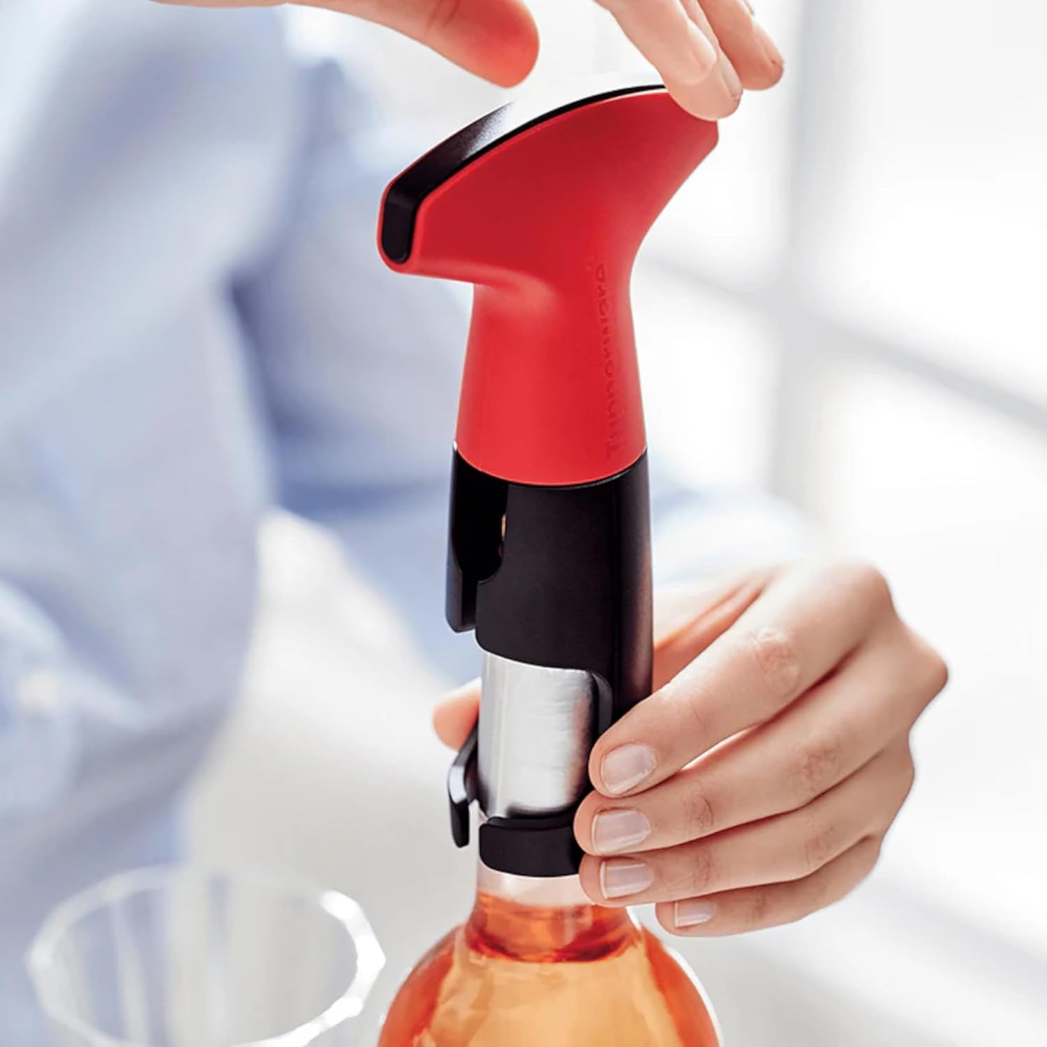Hands placing the red and black Tupperware Corkscrew D144 over the neck of a wine bottle.