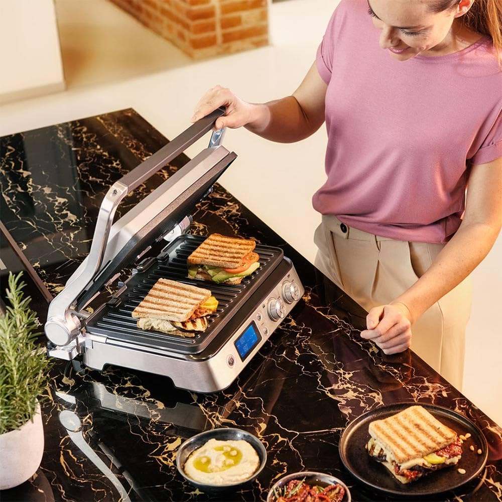 A person preparing grilled sandwiches on the Braun MultiGrill 9, which is open on a kitchen counter.