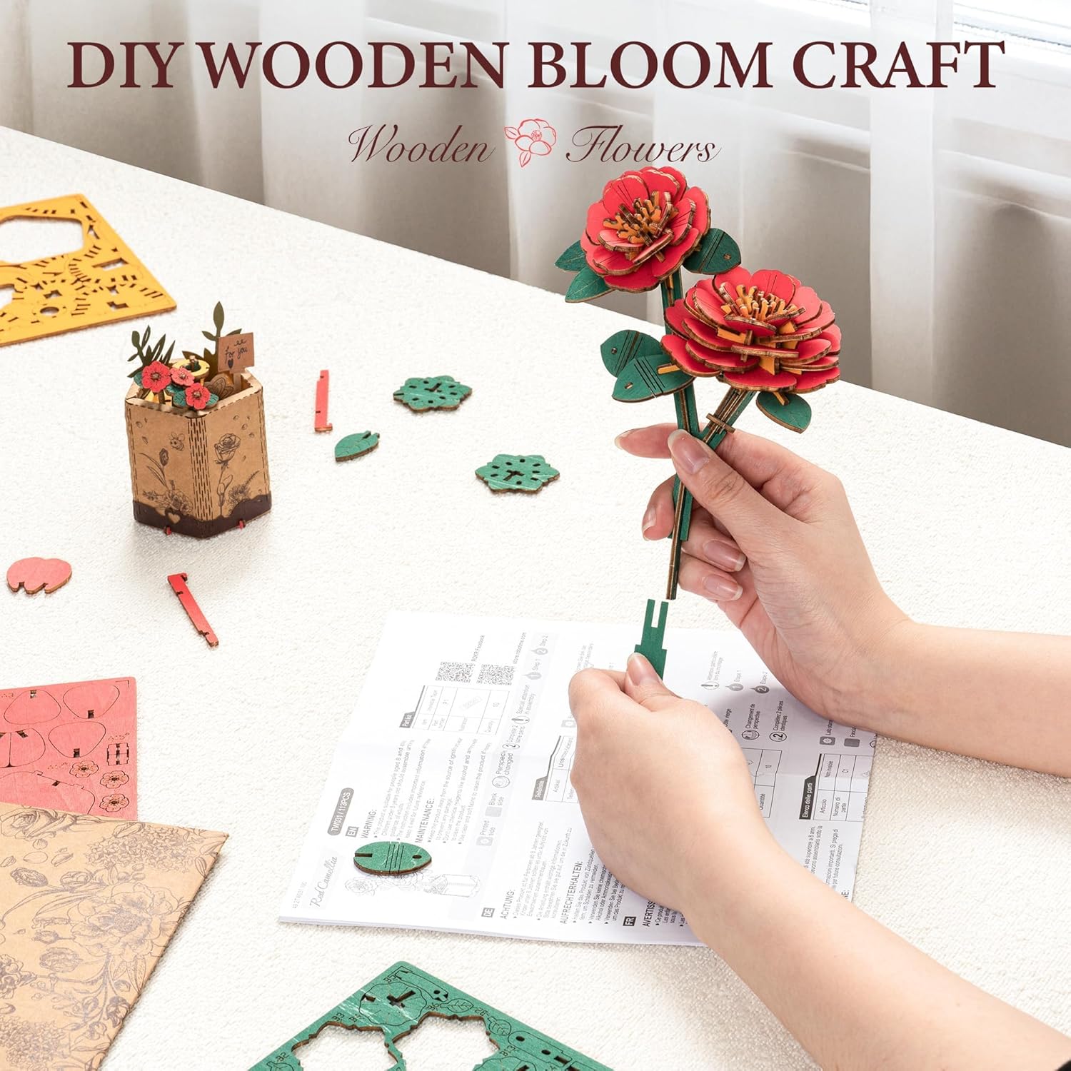 Hands assembling the wooden pieces of the Red Camellia flower puzzle, showing the process of attaching petals to the stem.