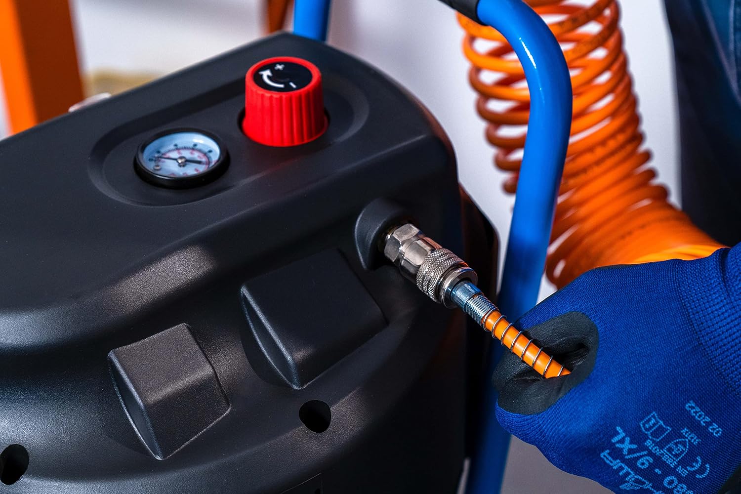 Close-up of a hand connecting an air hose to the quick coupler on the compressor.