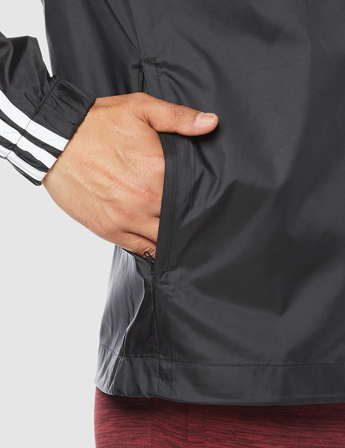 Detail shot of the Adidas Essentials 3-Stripes Woven Windbreaker, showing a hand in the zippered side pocket.