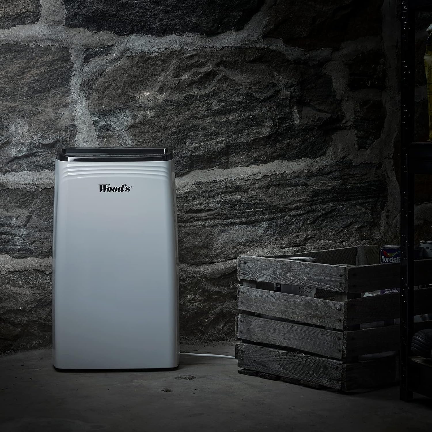 Wood's MDK 21 Dehumidifier placed in a basement or storage area with stone walls and wooden crates.
