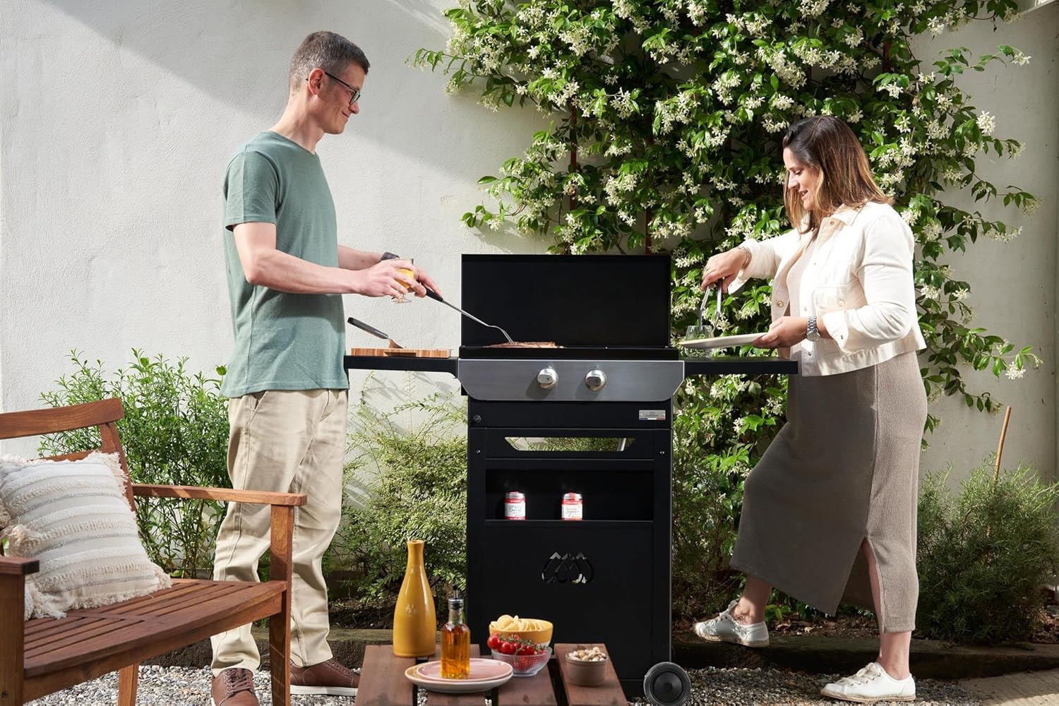 Two people cooking on the LE MARQUIER Plancha Original 260 Duo Edition in an outdoor setting