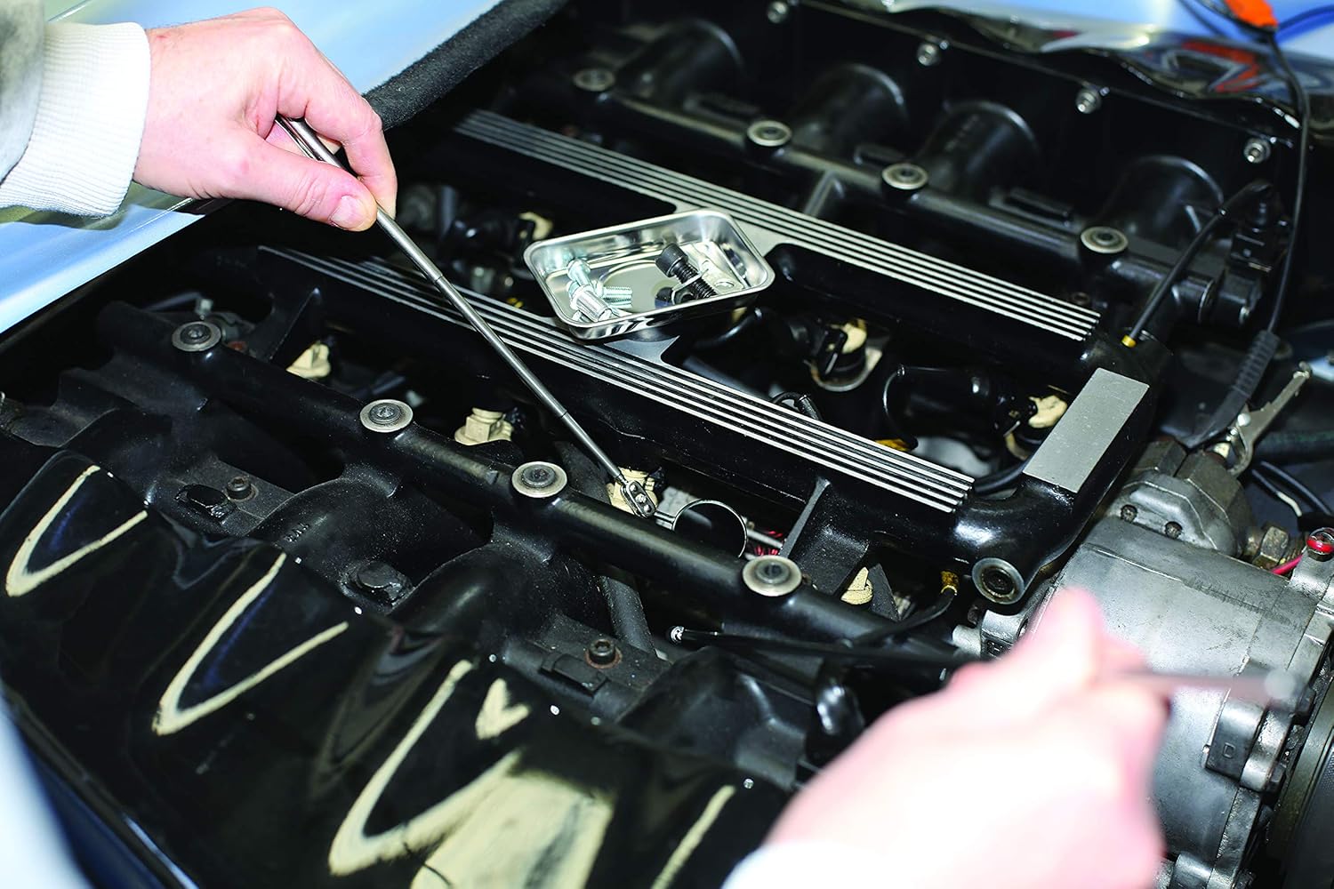 Hand using the magnetic pick-up tool to retrieve a small metal part from an engine compartment.