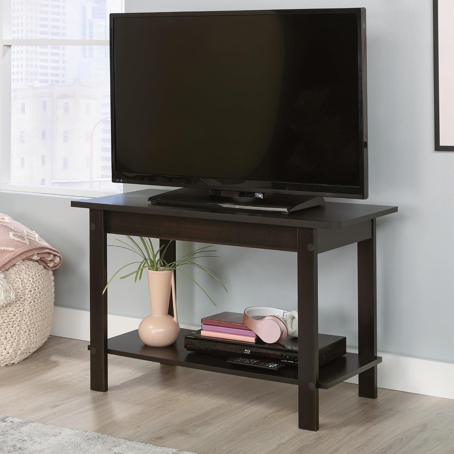 Sauder TV Stand with a television and decorative items on the lower shelf in a living space