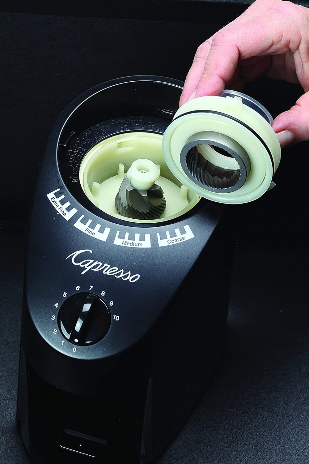 A hand removing the upper conical burr from the Capresso Infinity grinder for cleaning