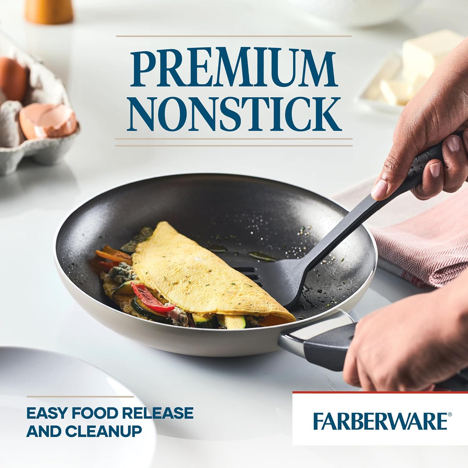 A hand using a spatula to easily slide an omelet out of a Farberware nonstick frying pan, demonstrating premium nonstick performance.