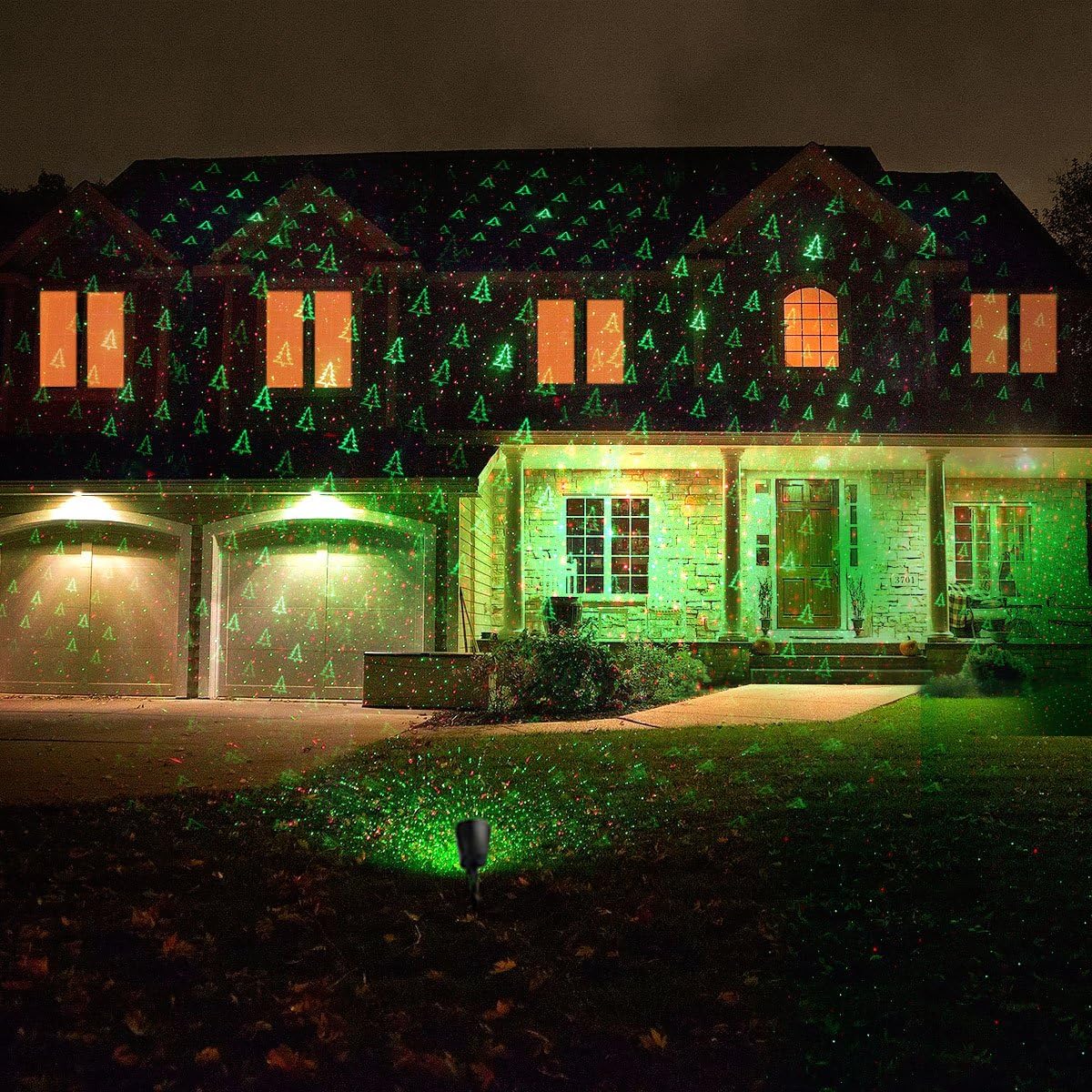 A house illuminated by green Christmas tree laser patterns from the 1 BY ONE projector placed in the foreground.