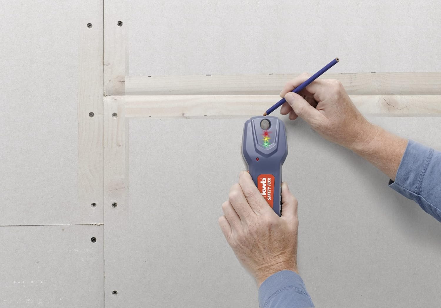 A hand holding the KWB Safety-Fixx detector and a pencil, marking the location of a wooden stud in a drywall.