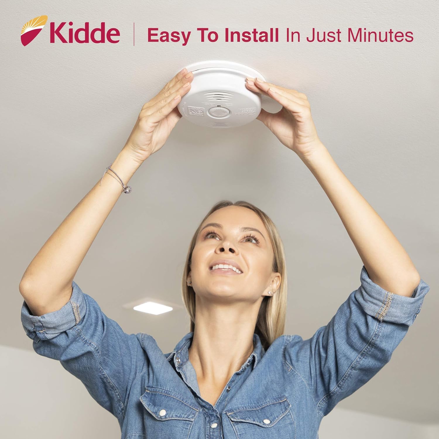 A person installing a Kidde i12010SCO alarm on a ceiling.