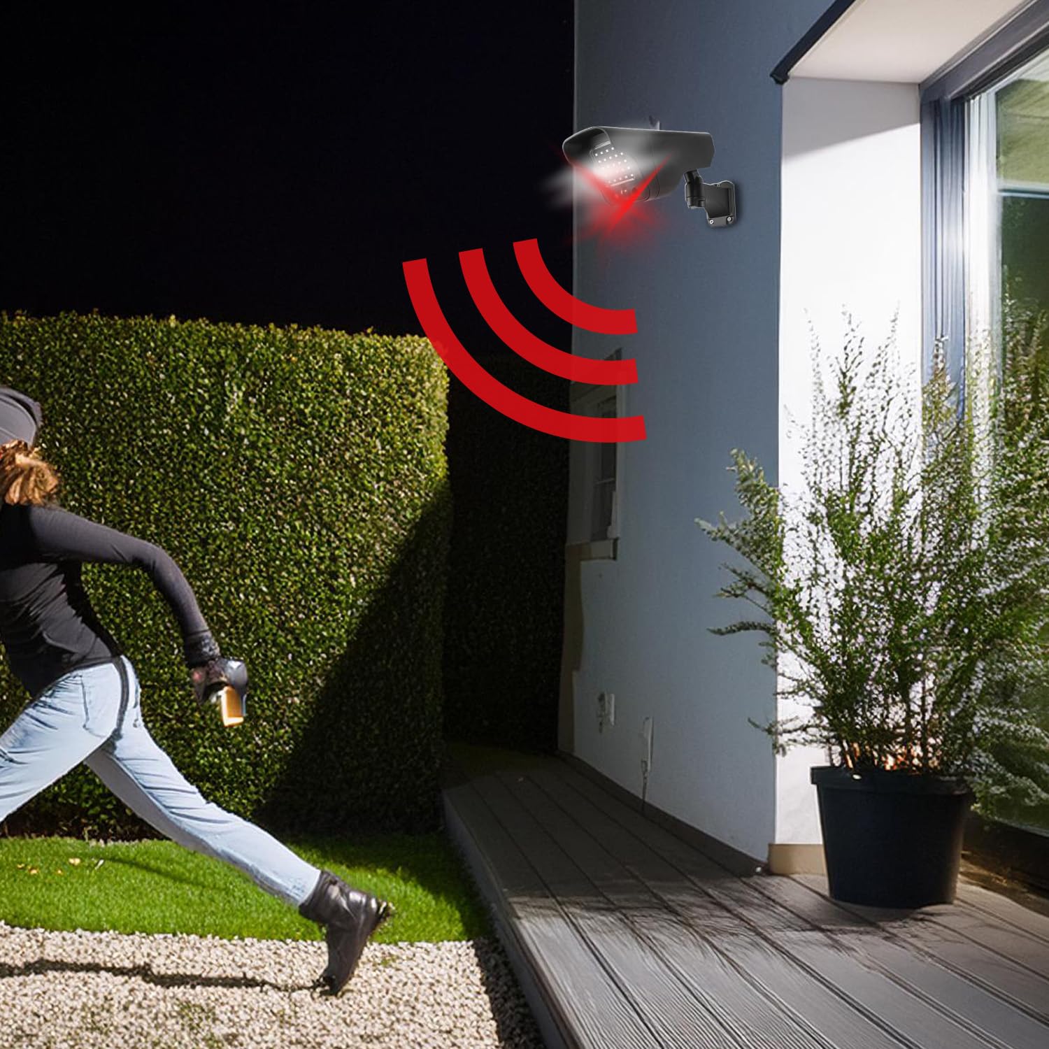 Image depicting the dummy camera mounted on a wall at night, with red light waves emanating from it, indicating motion detection and deterrence as a person runs past.