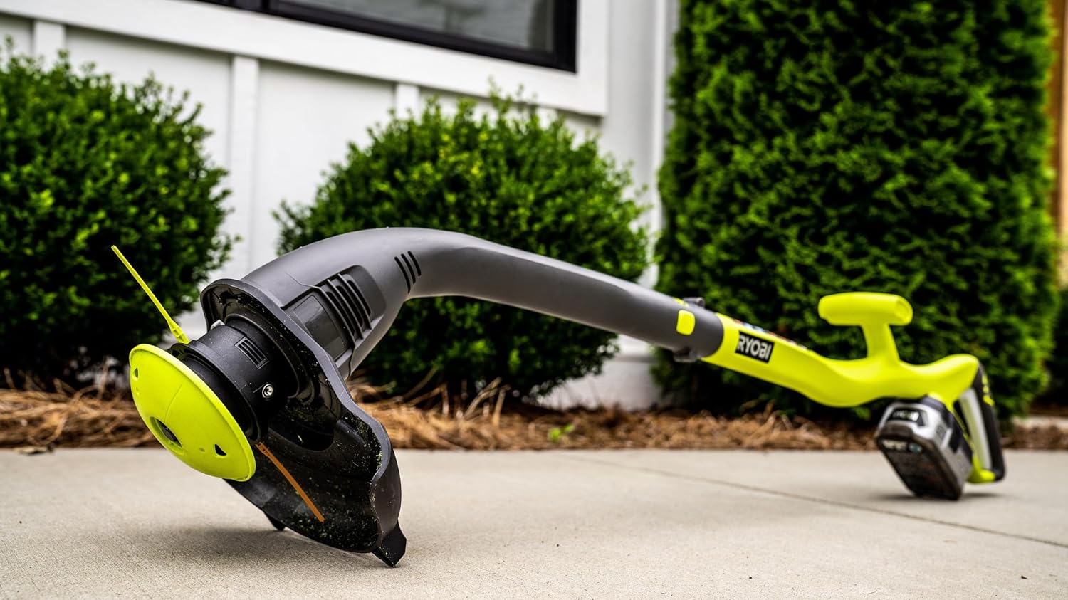 A person using a Ryobi string trimmer equipped with the Aero-Flex Snap & Trim head to trim grass along a fence line.