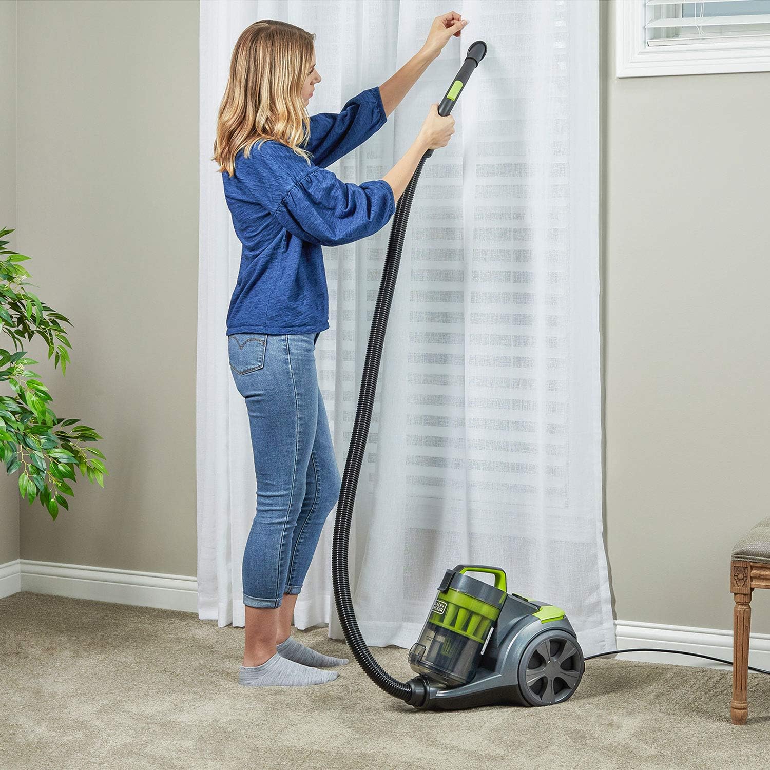 User vacuuming curtains with the extension wand and a small brush attachment