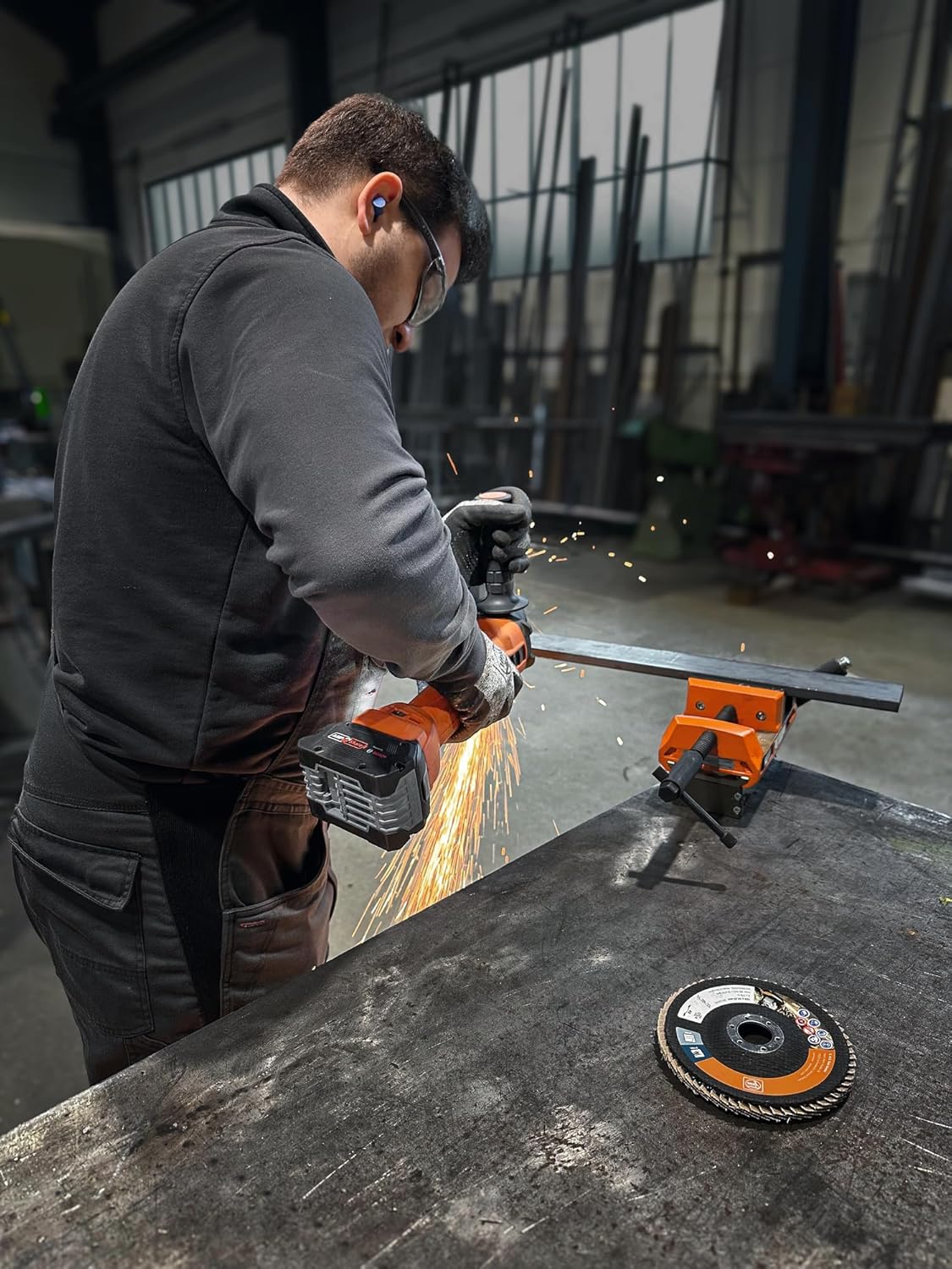 Man using Fein Cordless Angle Grinder CCG 18-115-12 AS to cut a metal bar, sparks flying.