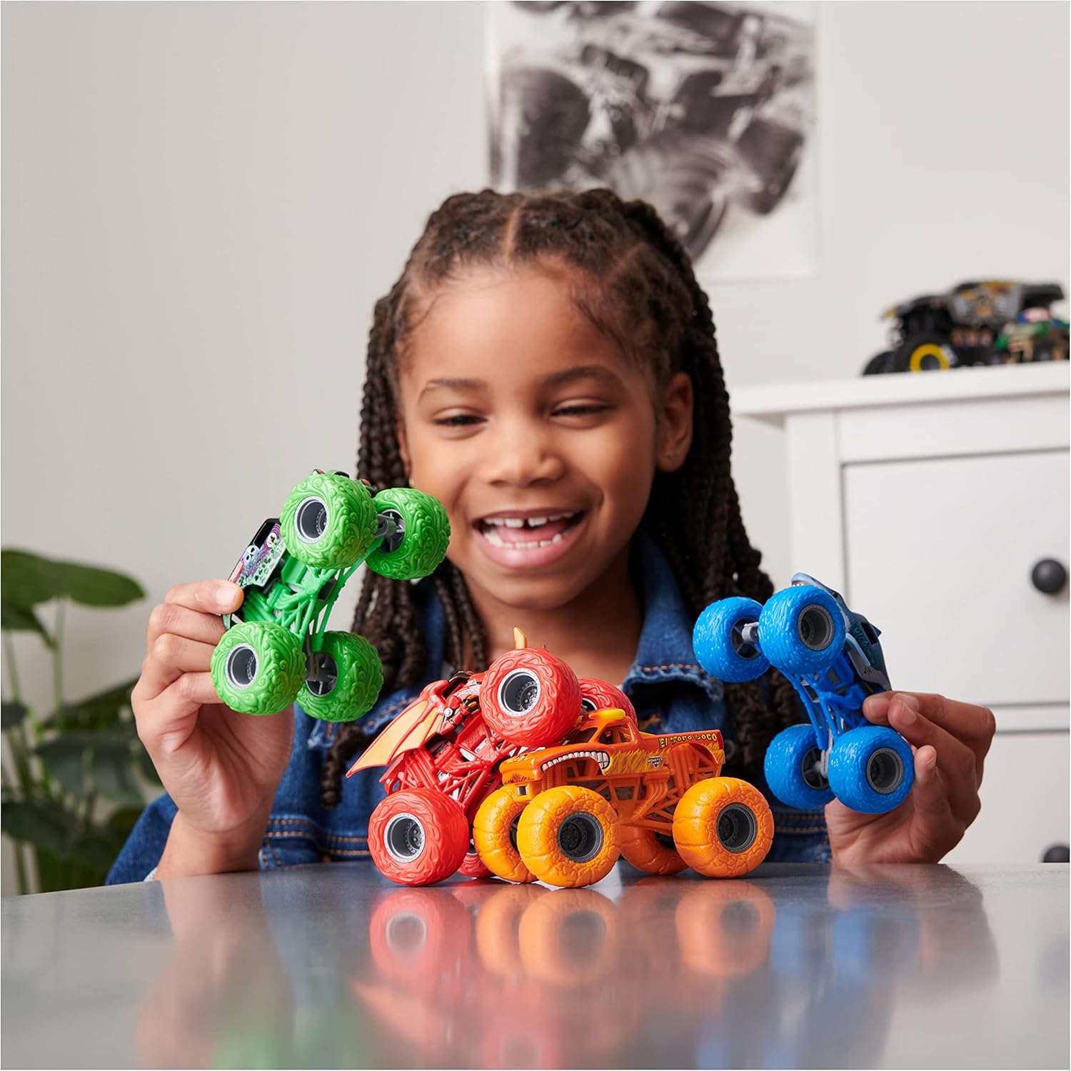 A child happily playing with three Monster Jam trucks on a table.