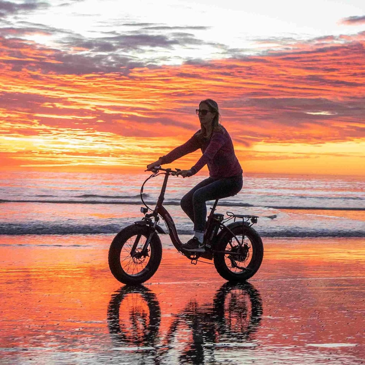 Person riding EMOJO Ram SS electric bike on a beach at sunset.