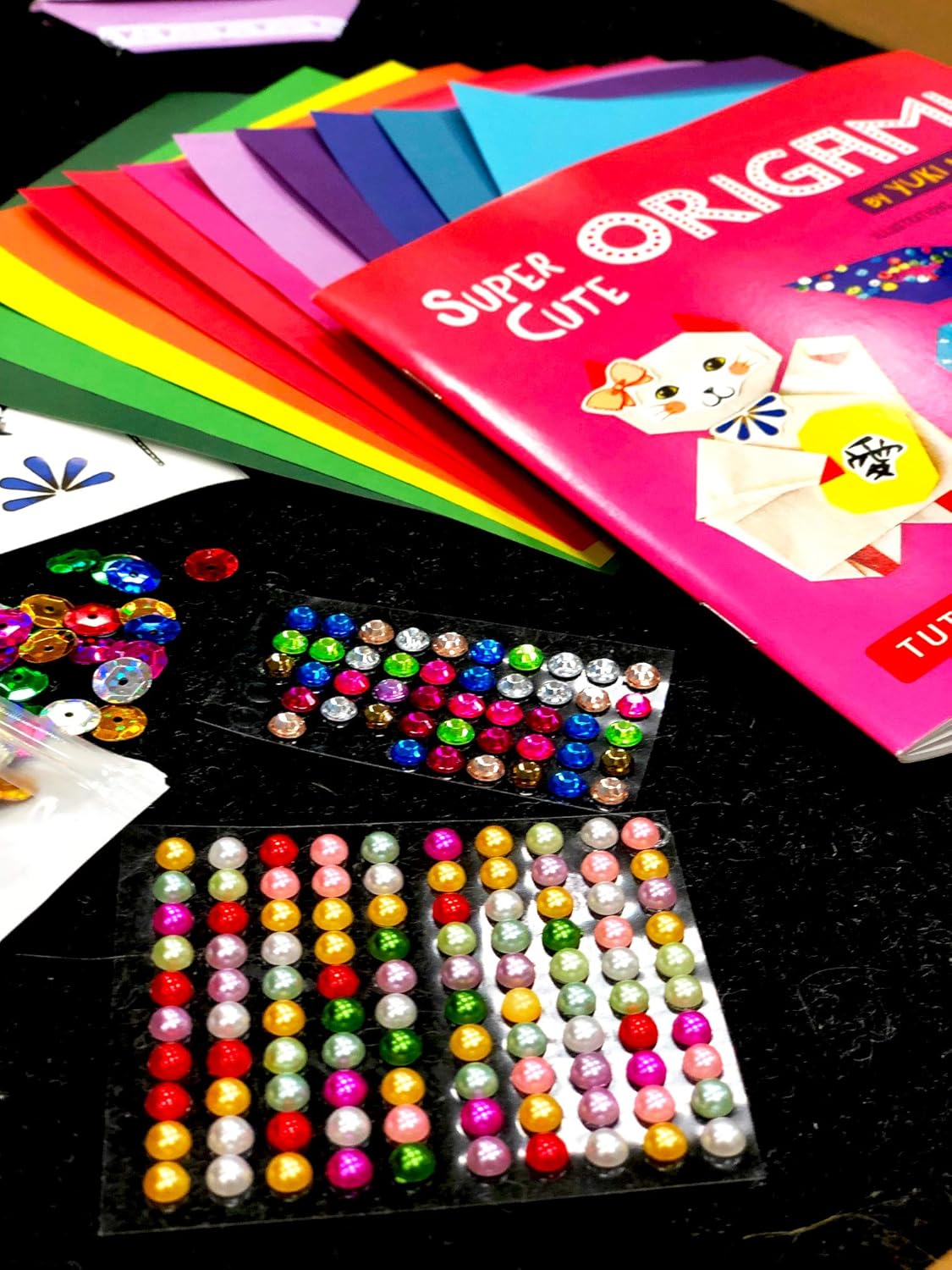 Close-up of stick-on pearls and glittering sequins in various colors, included in the origami kit.