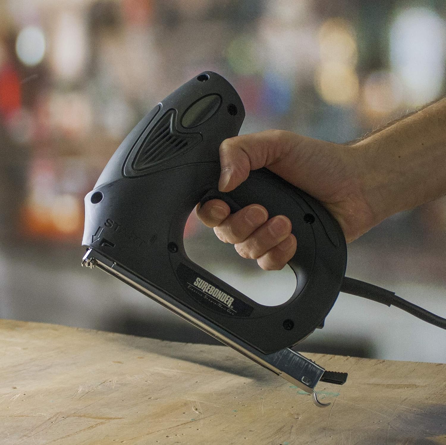 A hand holding the Surebonder 5900N Electric Staple Gun in an operating position, ready to fire.
