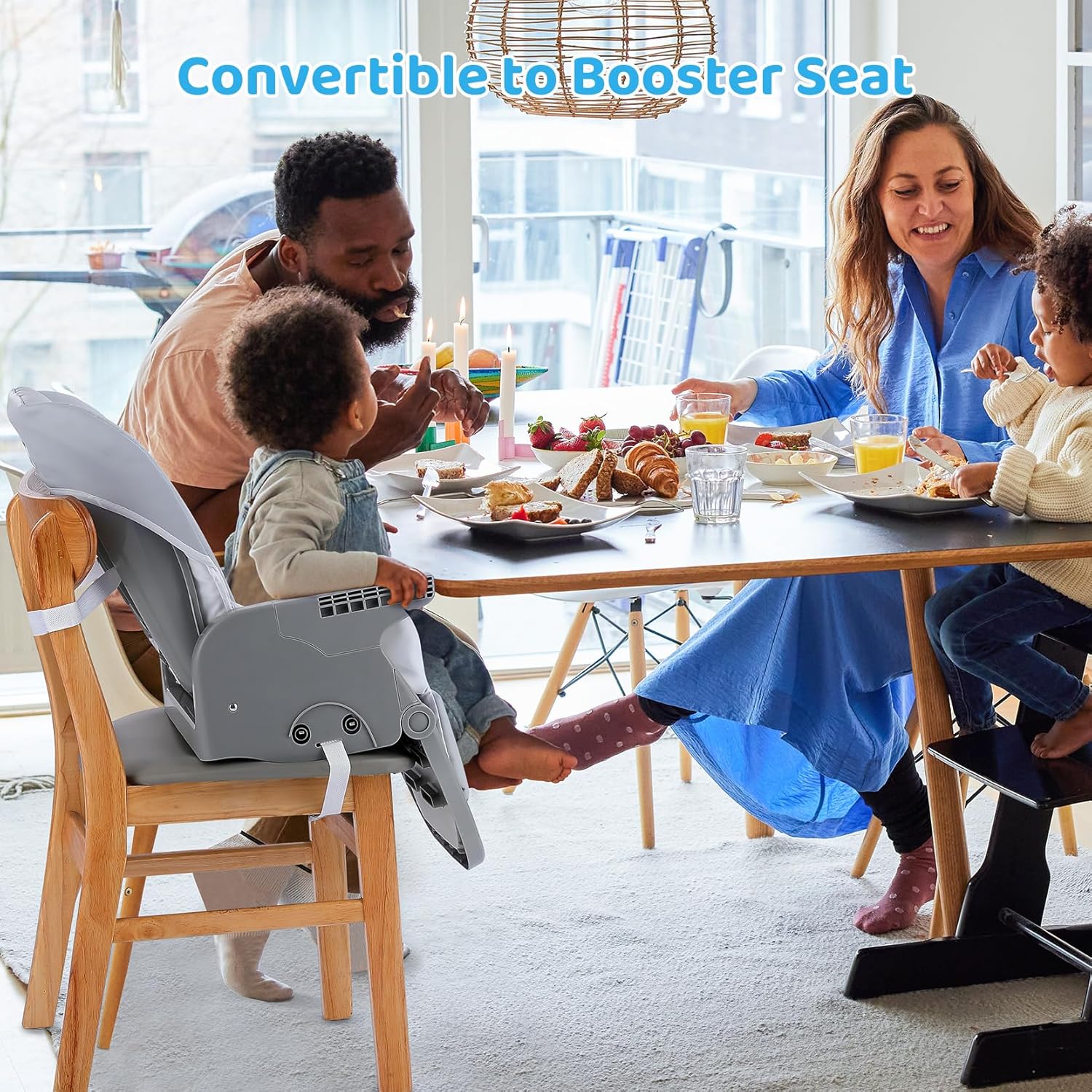 A baby in the Ezebaby high chair seat, converted into a booster seat and strapped to an adult dining chair at a family meal.