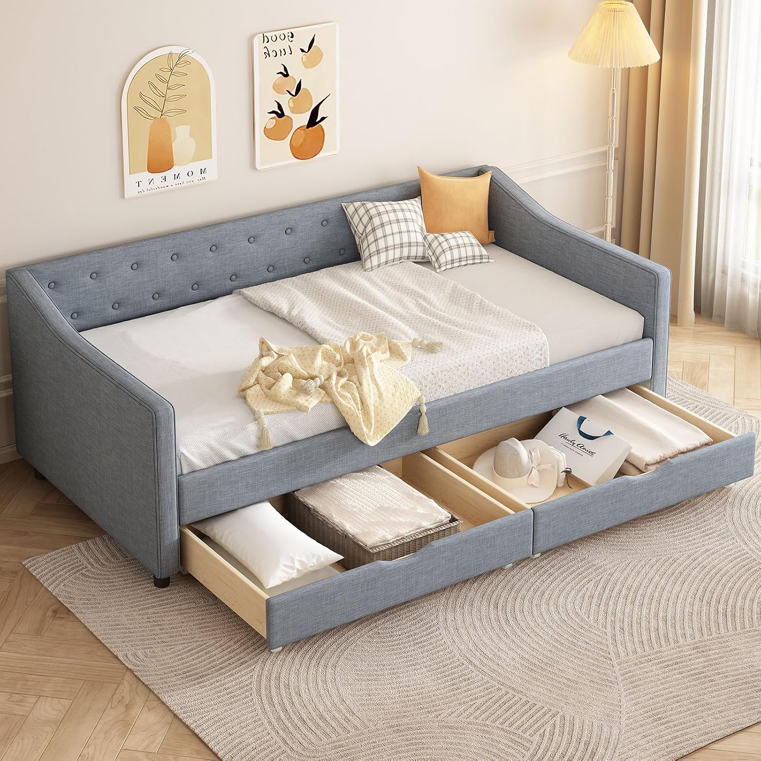 A light grey velvet upholstered twin daybed with two storage drawers, shown in a room setting with a mattress and pillows.