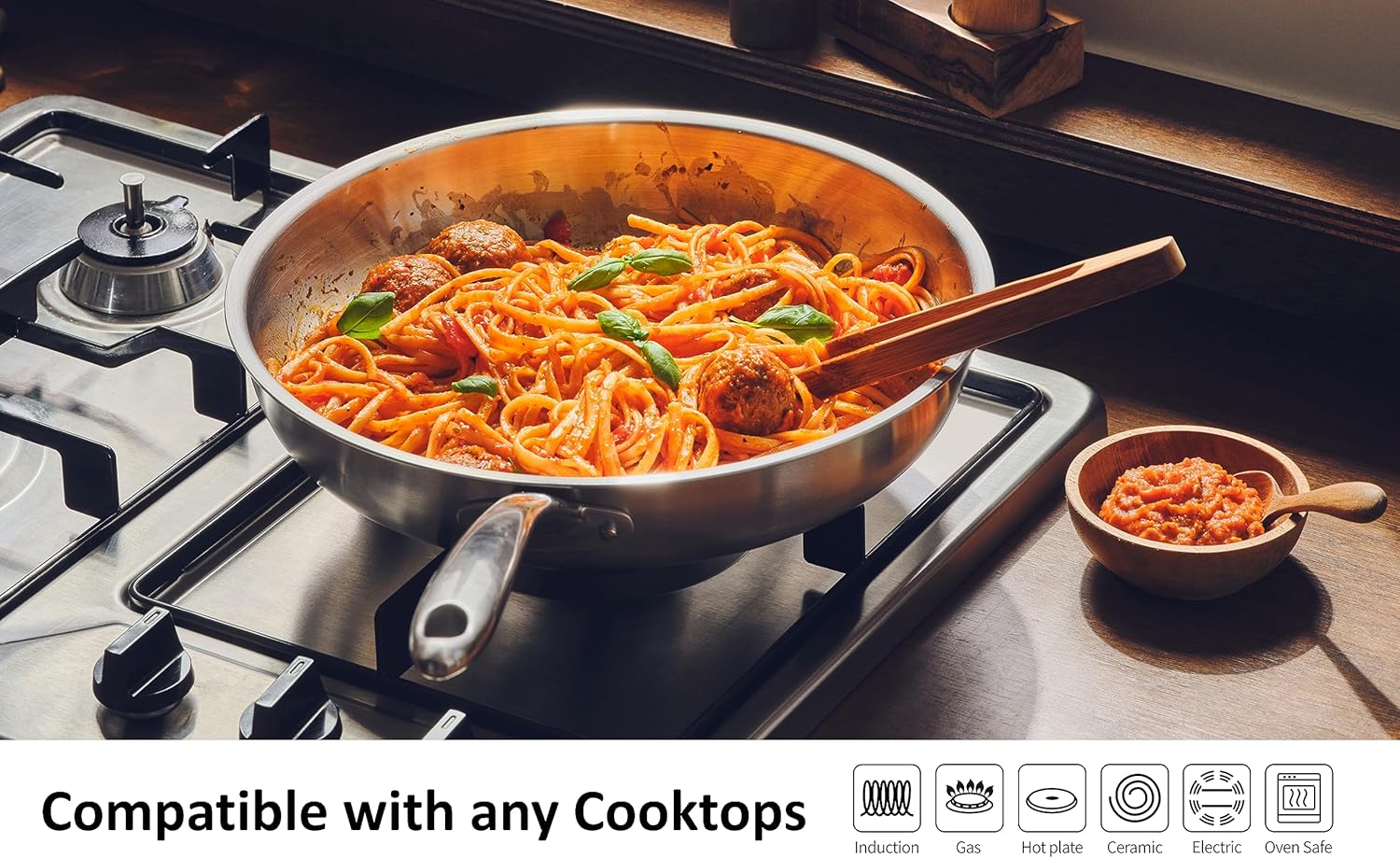 Frying pan on a gas stovetop with pasta and meatballs, showing cooktop compatibility icons