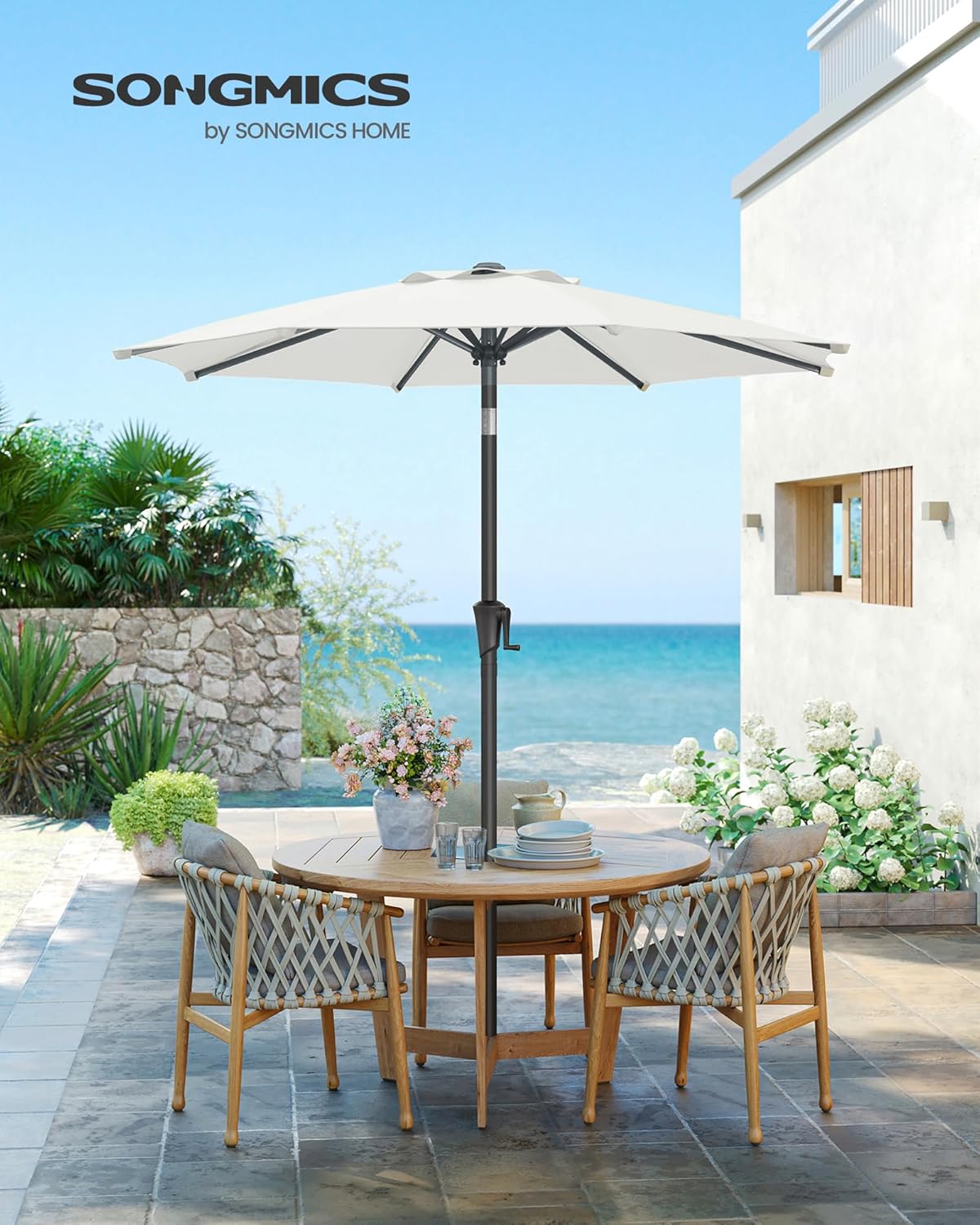 SONGMICS 9 ft Patio Umbrella set up on a patio next to a table and chairs, with a beach in the background.
