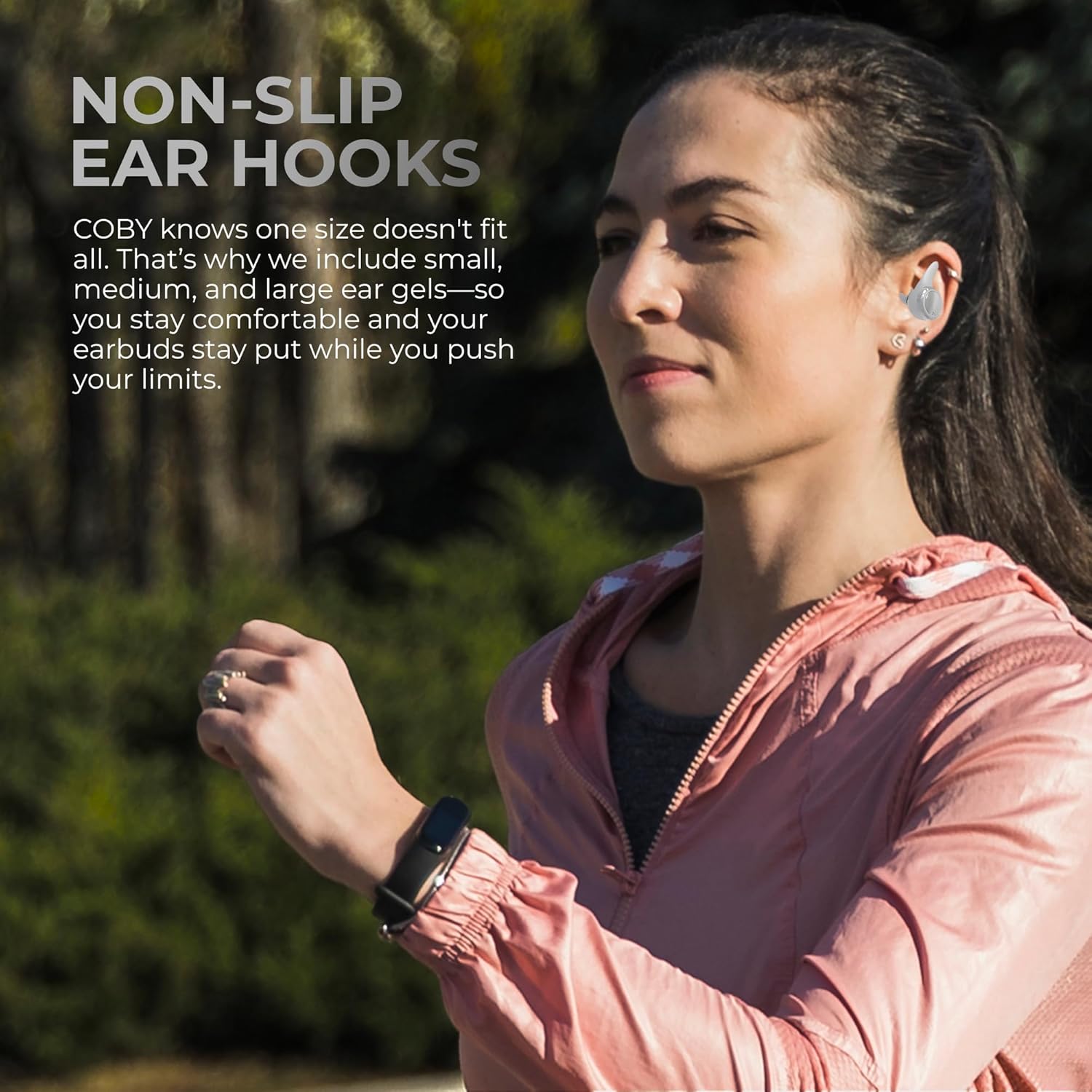 Woman running outdoors wearing Coby earbuds with non-slip ear hooks.
