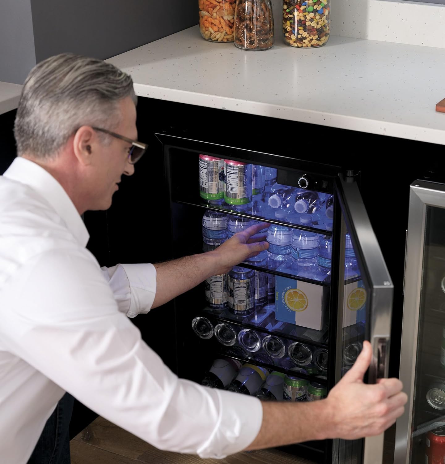 Man arranging water bottles on a shelf inside the Haier mini fridge