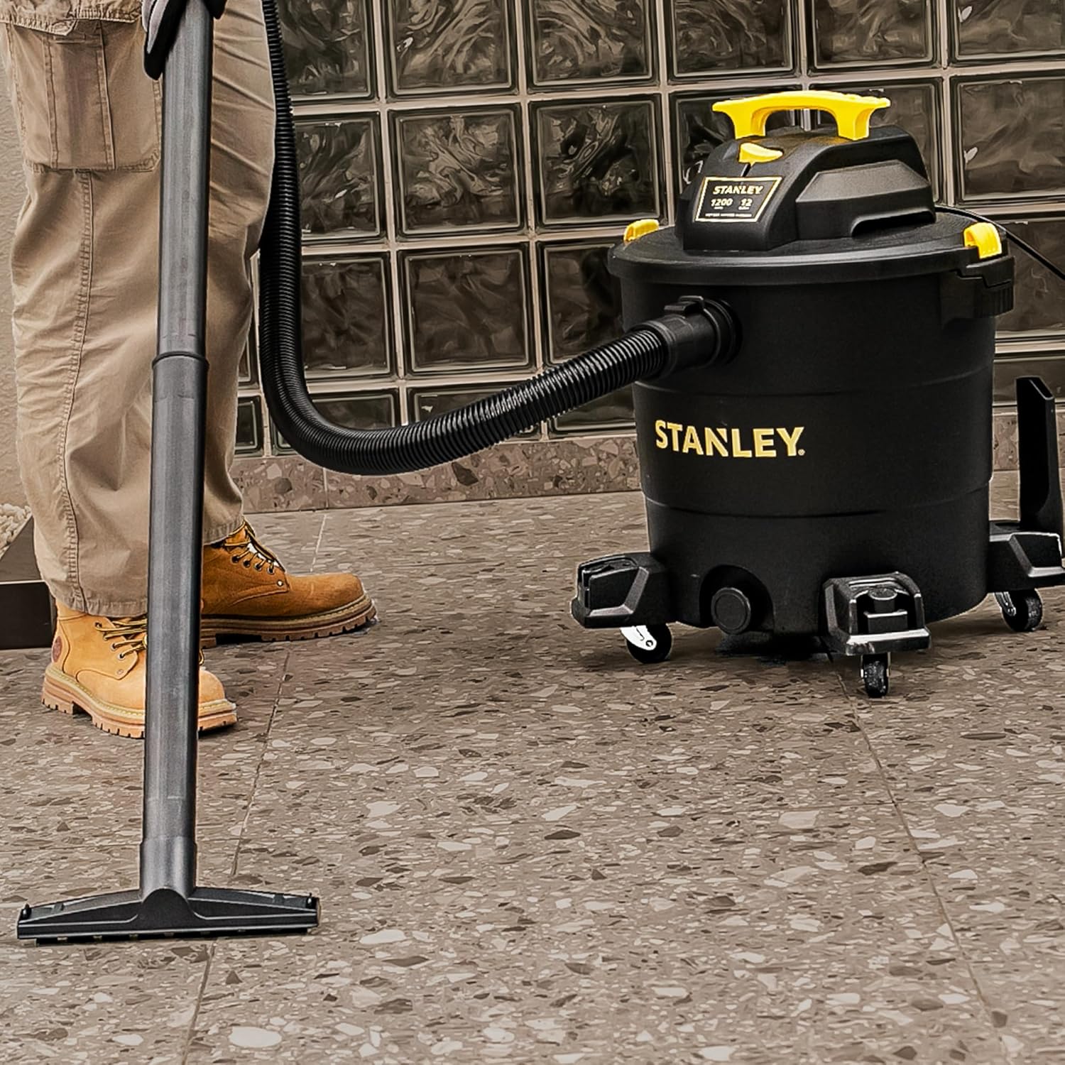 Person using the floor nozzle of the STANLEY wet/dry vacuum to clean a garage floor with sawdust