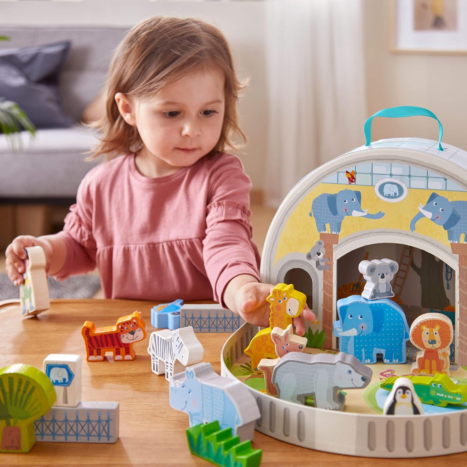 A child playing with the HABA wooden zoo playset, arranging animal figures