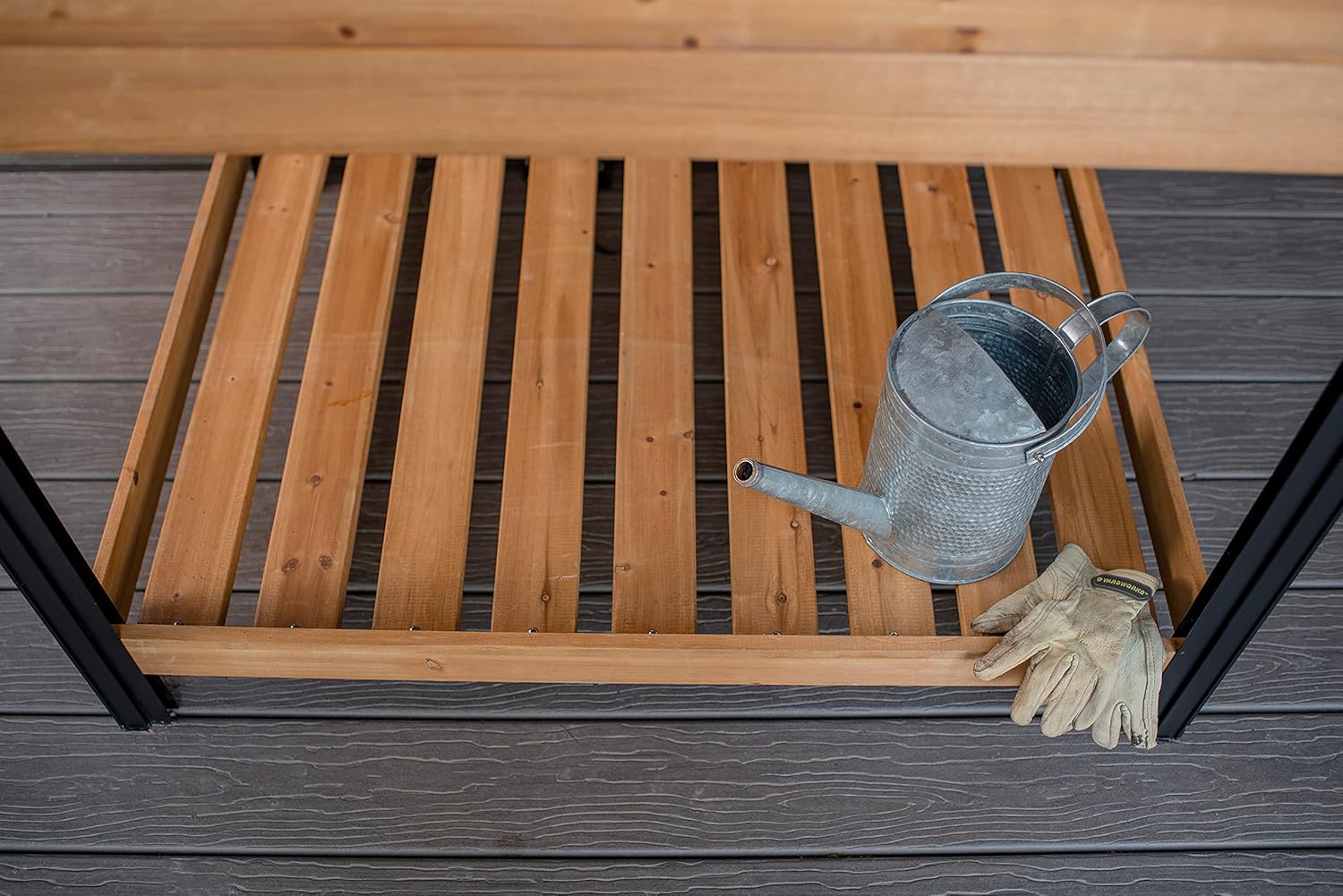 Close-up of the bottom storage shelf with a watering can and gardening gloves