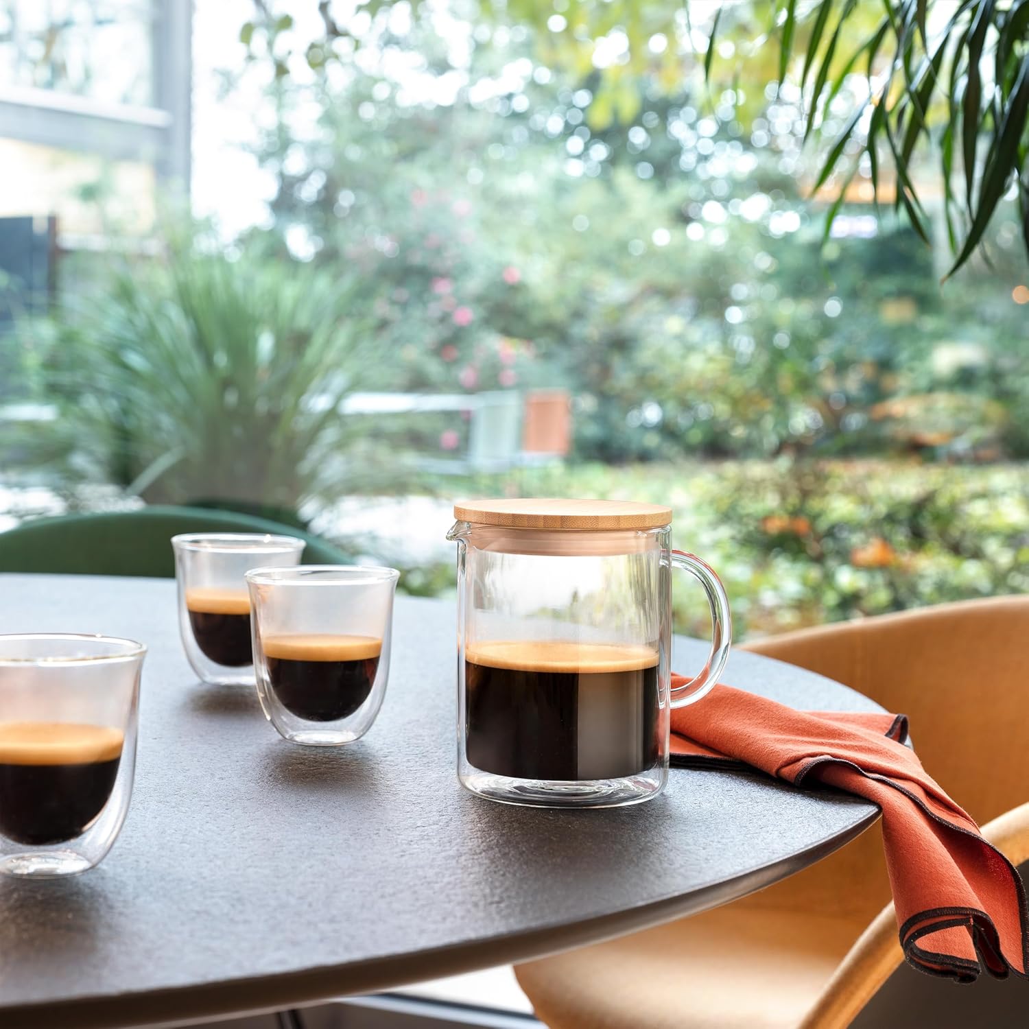 De'Longhi Double Wall Glass Coffee Pot filled with coffee, placed on a table with two smaller double-wall glasses, ready for serving.