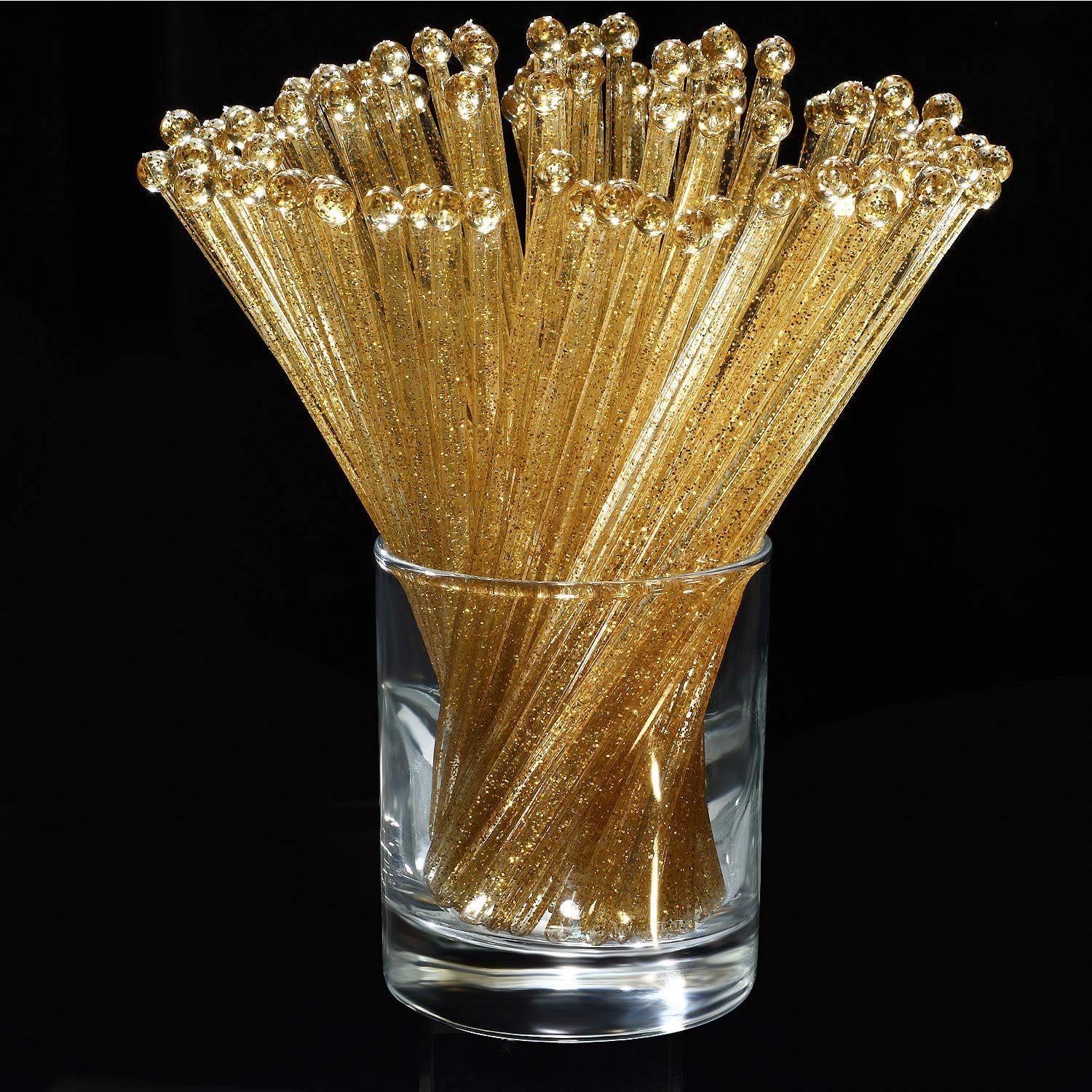 Clear cup filled with 100 gold, sparkly plastic swizzle sticks for mixing drinks.