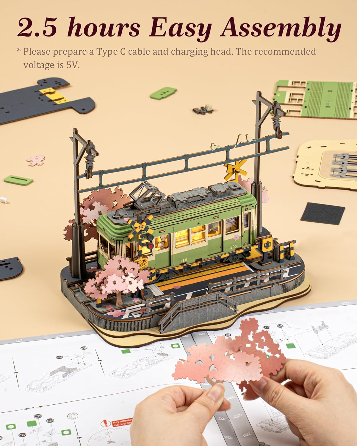 Hands assembling parts of the ROBOTIME Sakura Journey 3D Wooden Tram Model Kit, showing the intricate process