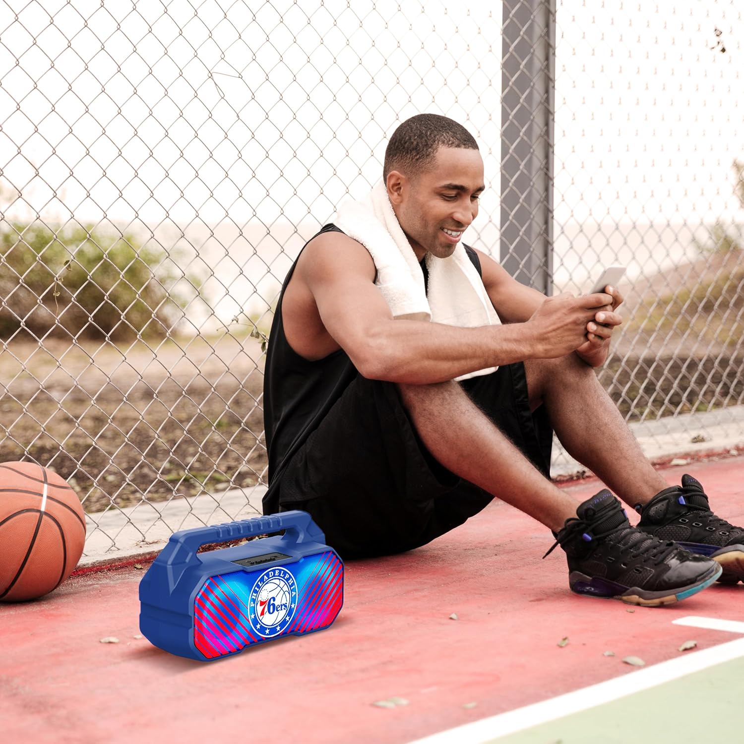 A group of friends sitting around the SOAR NBA Wireless Boombox Speaker in a dimly lit setting, with the speaker's LED lights illuminated.