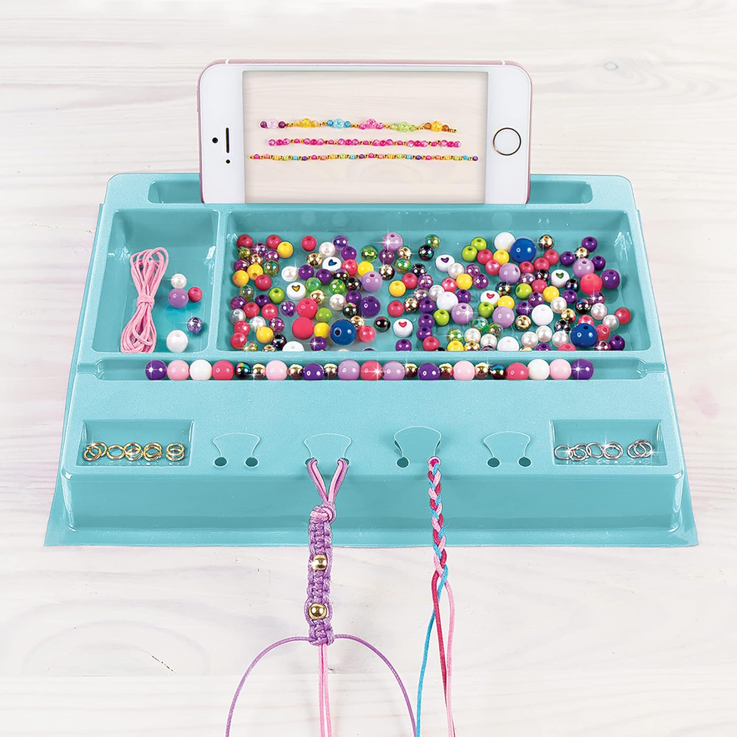 A blue bead mat with various colorful beads and cords, and a smartphone resting in a designated slot.