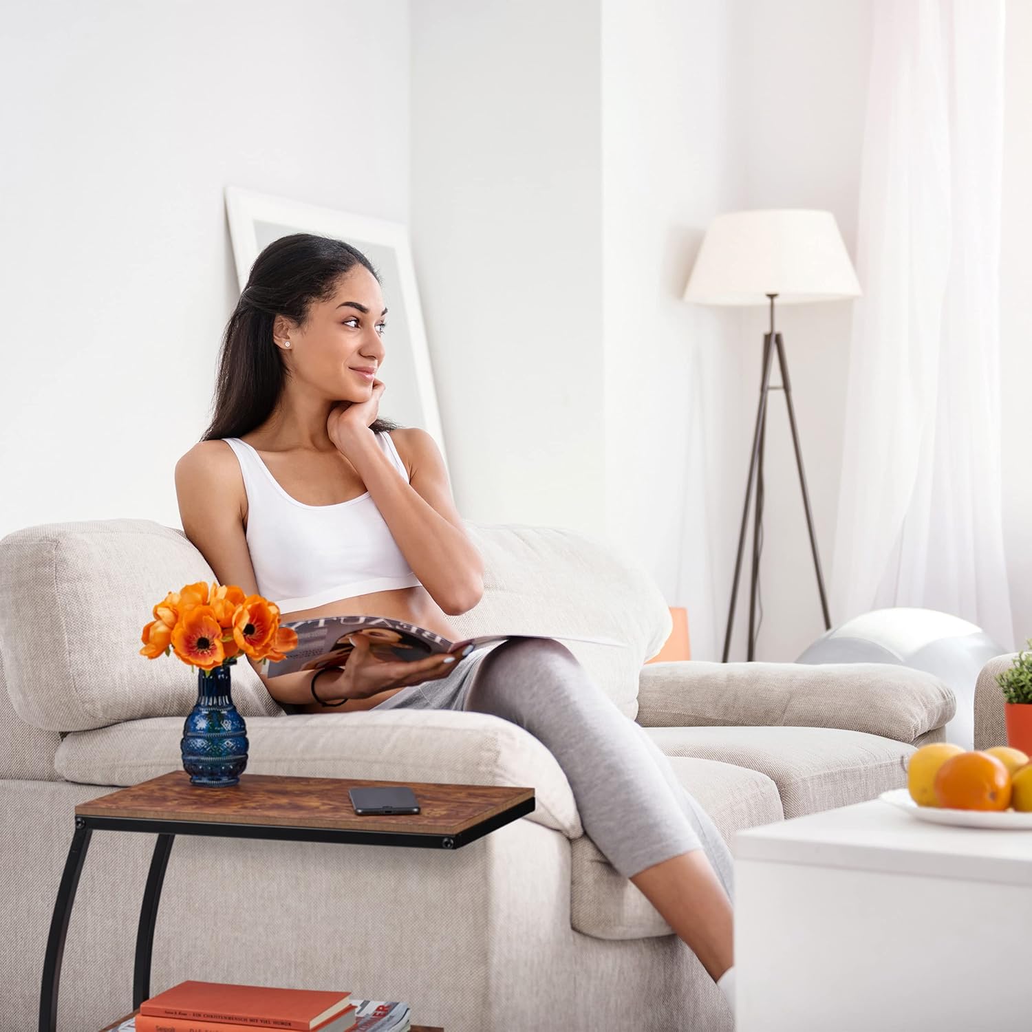 A woman relaxing on a light-colored sofa, with the Relaxdays C-shaped Side Table next to her, holding a phone and a small vase.